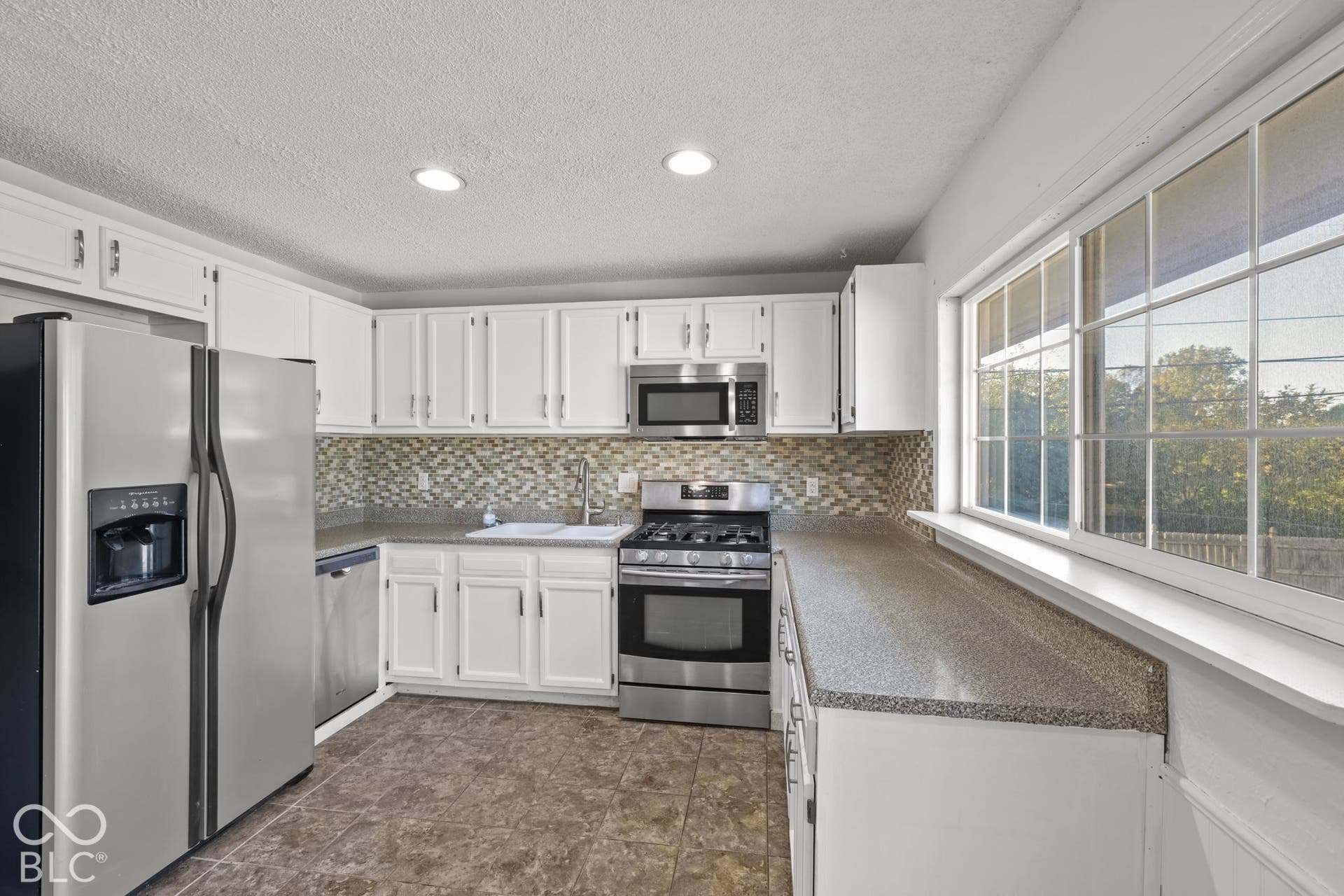Kitchen featuring white cabinetry, stainless steel appliances, mosaic tile backsplash, and a large window