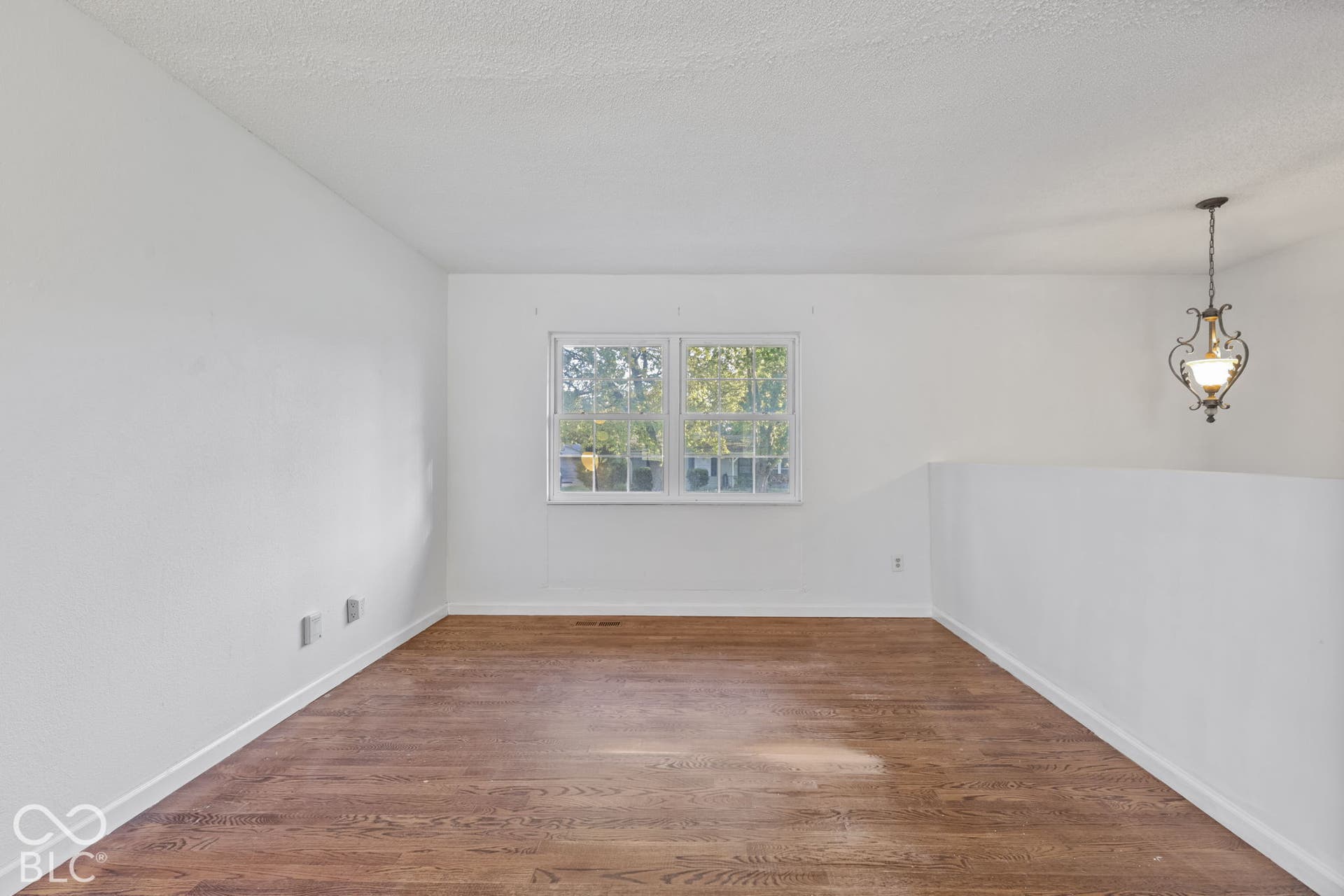 Wood-finish flooring, single window, white walls, built-in half-wall, and a hanging light fixture