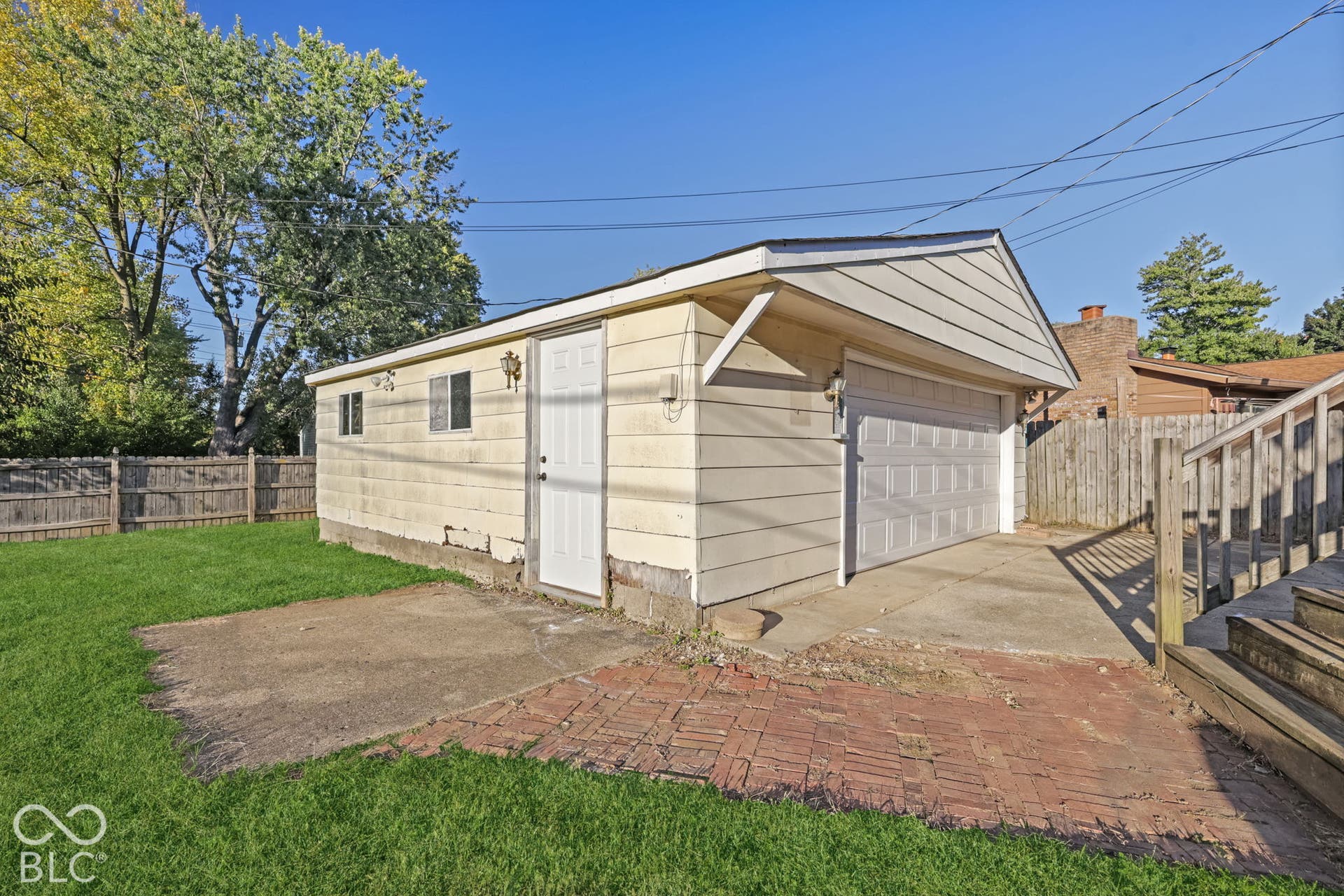 Virtually Altered - Detached garage with a single overhead door, an exterior door, two windows, and a paved concrete driveway