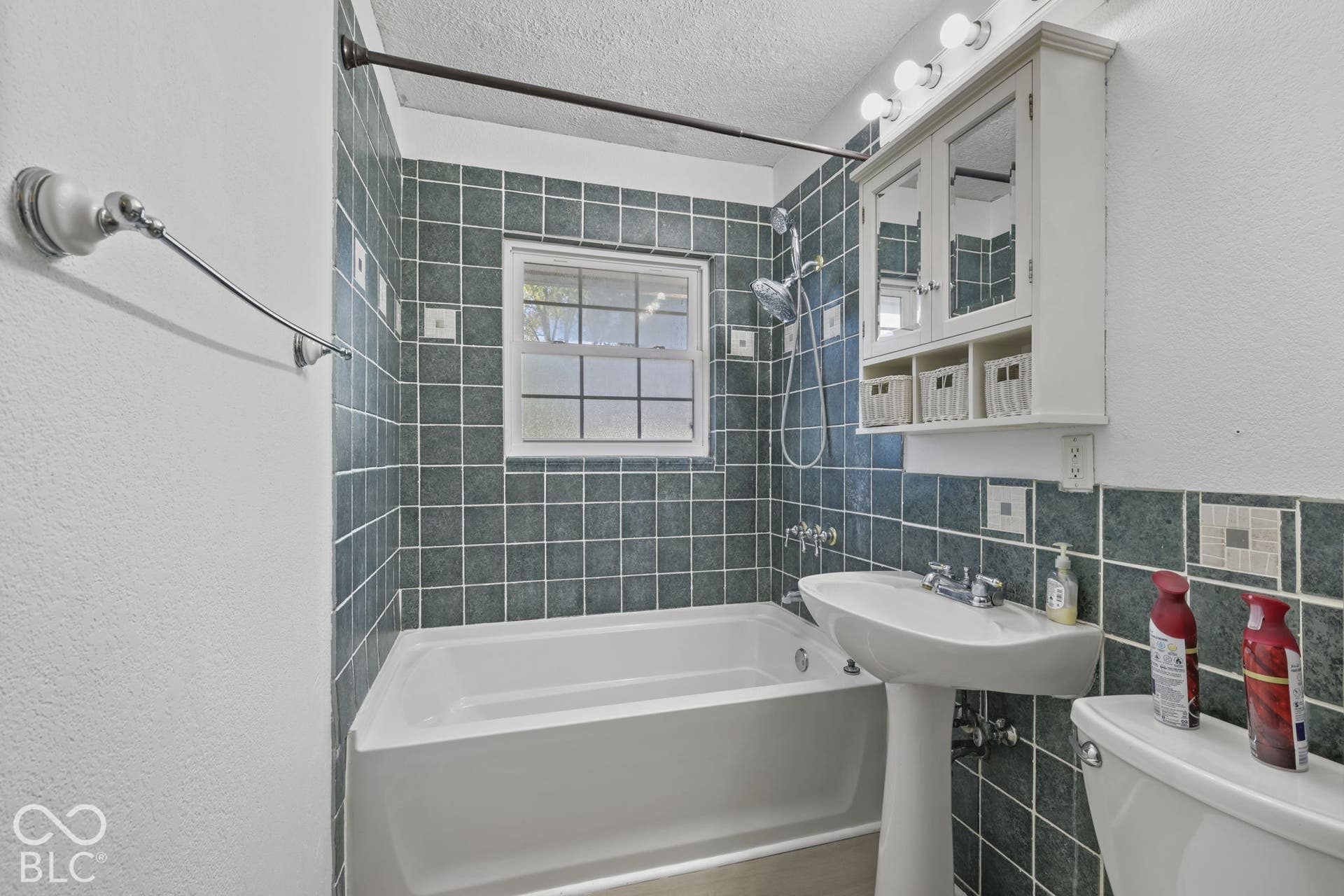 Bathtub with a shower fixture, pedestal sink, wall-mounted medicine cabinet with integrated lighting, and tile surround