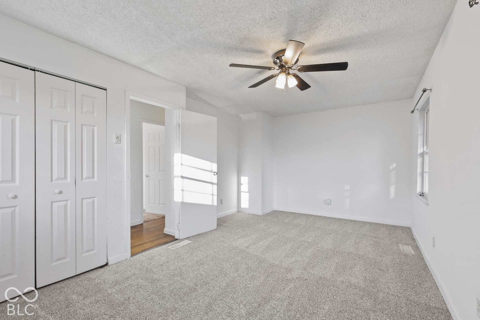 Light gray carpeting with a ceiling fan light fixture, white walls, and a window with a curtain rod