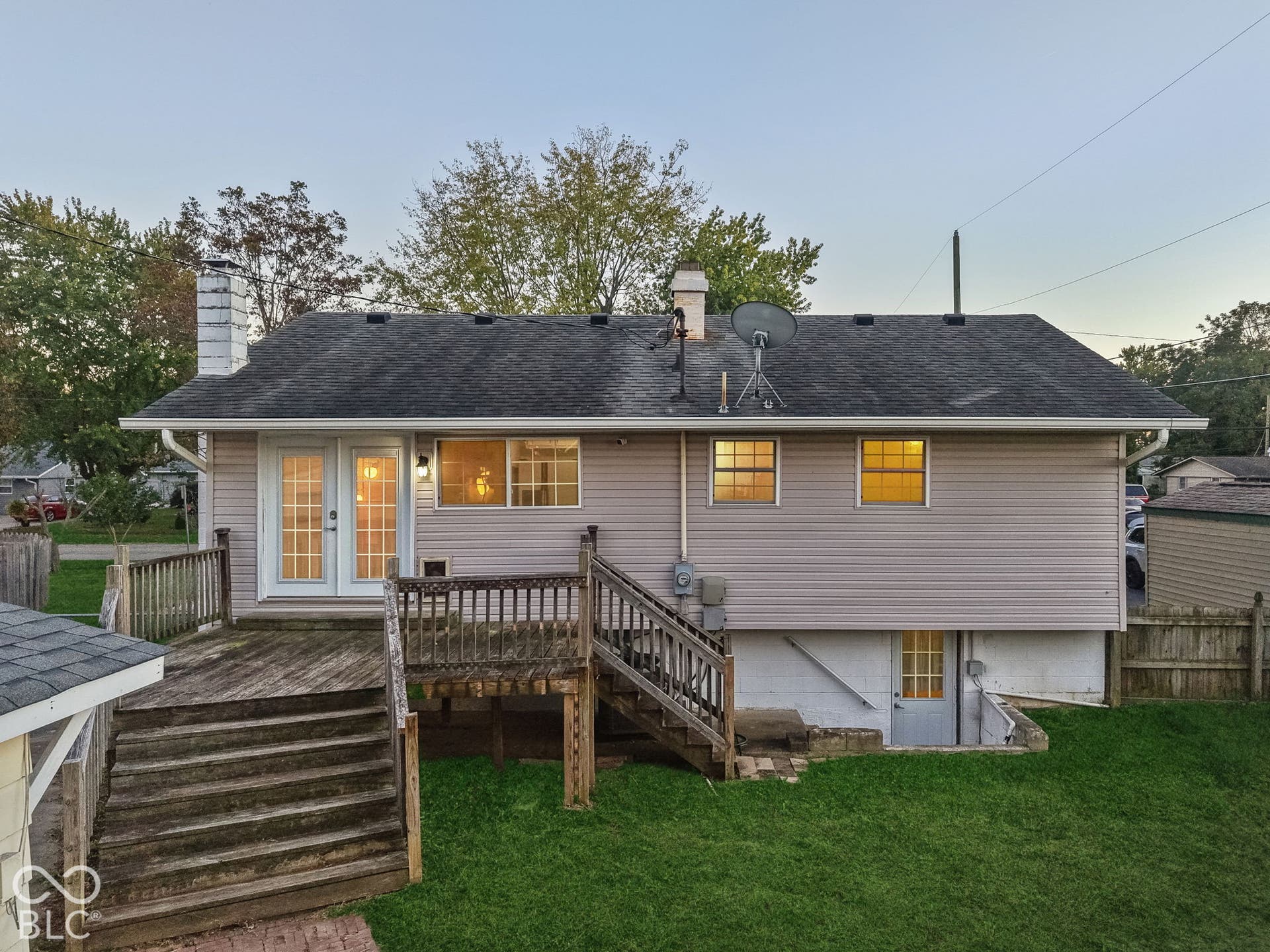 Virtually Altered - Expansive rear deck featuring double French doors, a lower-level entry, and a manicured lawn