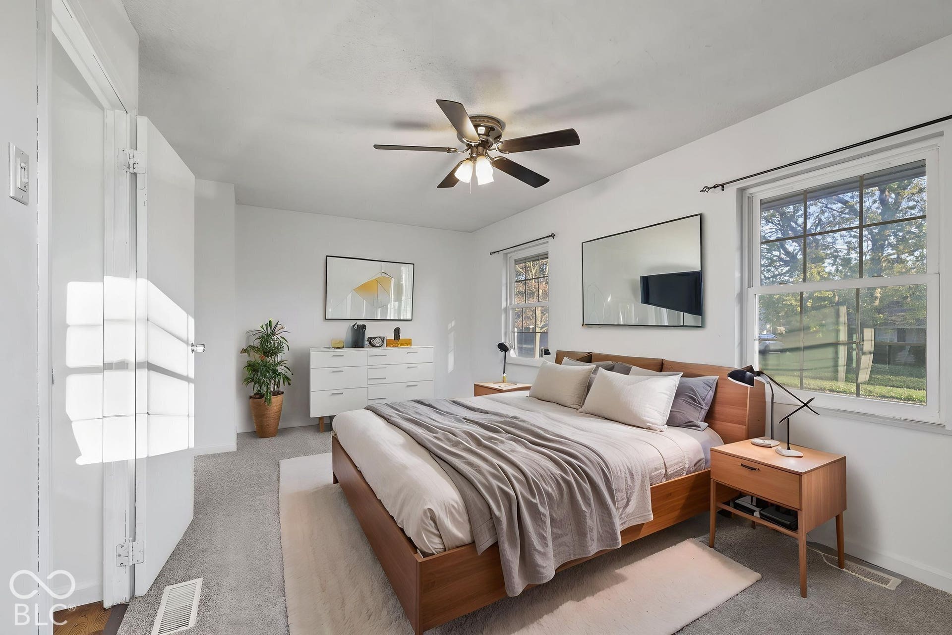 Virtually Altered - Carpeted bedroom featuring a ceiling fan with integrated lighting, two double-hung windows, and a built-in closet