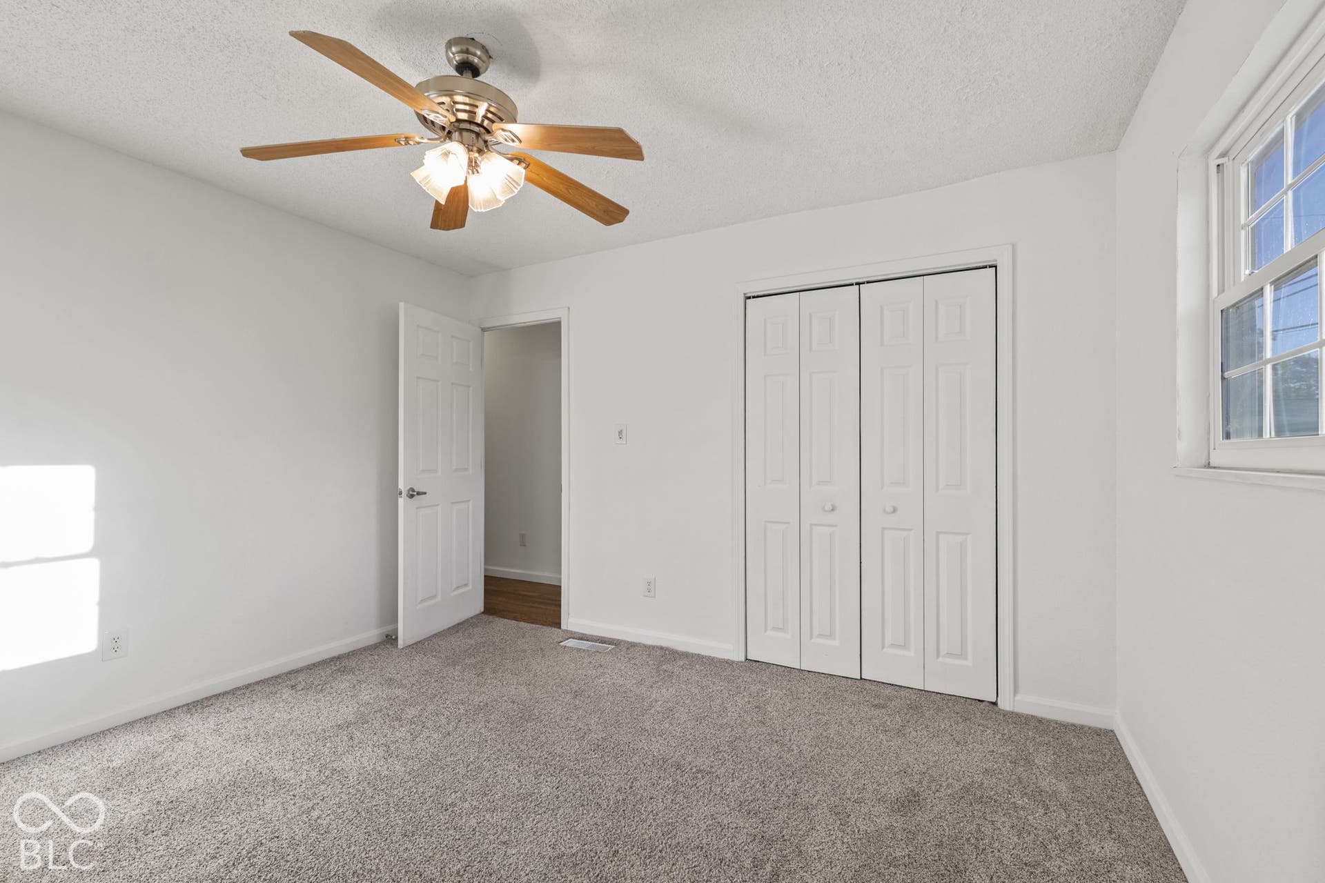 Recessed window with white trim, bi-fold closet doors, ceiling fan with integrated lighting, and neutral carpeting