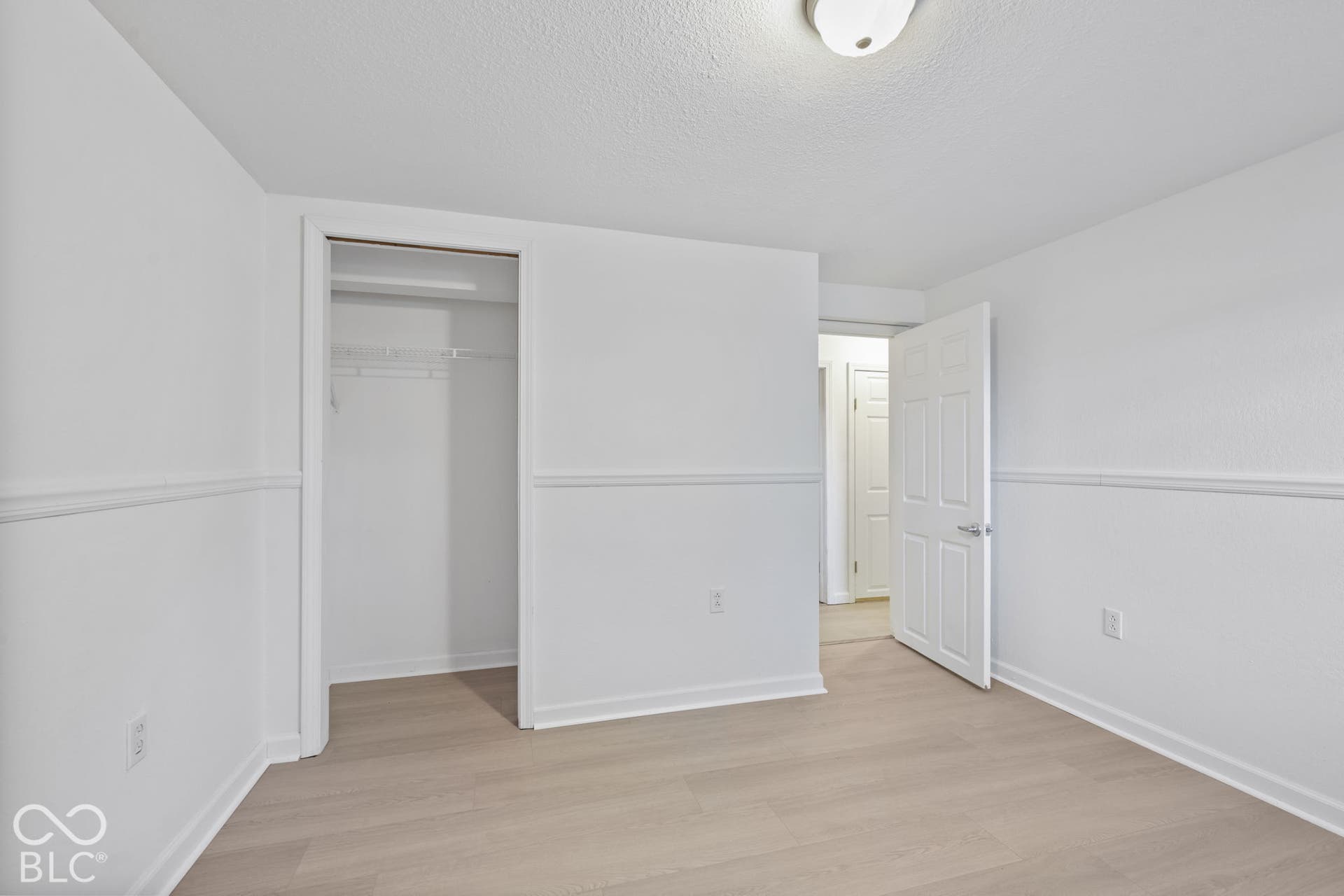 Wood-finish flooring, white walls with chair rail molding, and a built-in closet with wire shelving