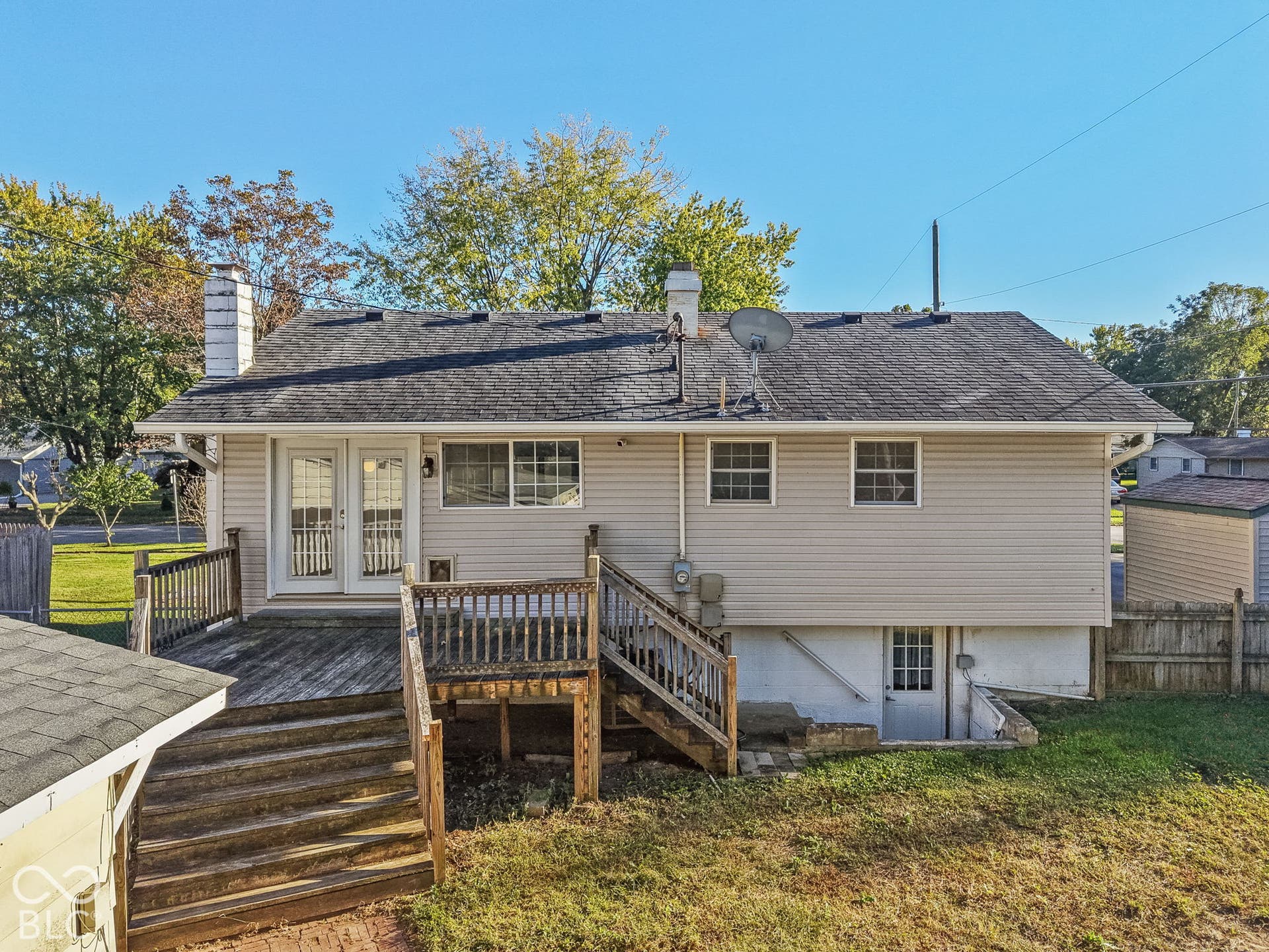 Rear exterior featuring a spacious wooden deck with railings, two double-paned windows, and a lower-level access door