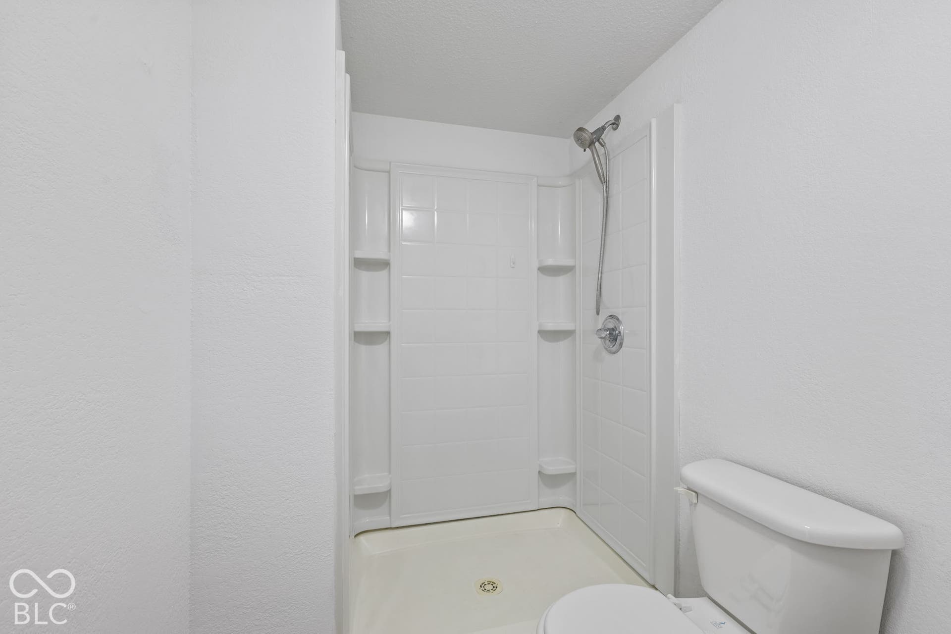 Shower stall with white tiled walls, integrated shelving, and a chrome shower fixture