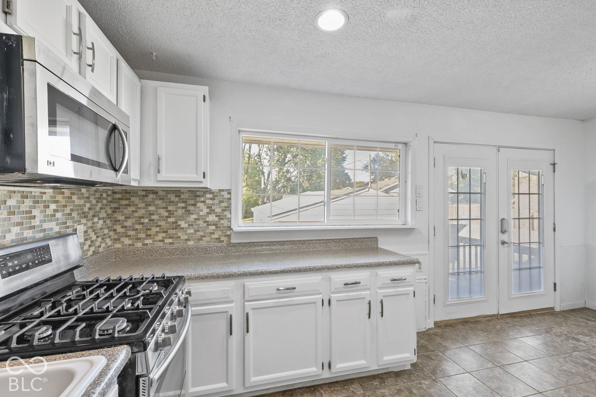 White cabinetry, tile backsplash, stainless steel appliances, dual glass-paneled doors, and tiled flooring