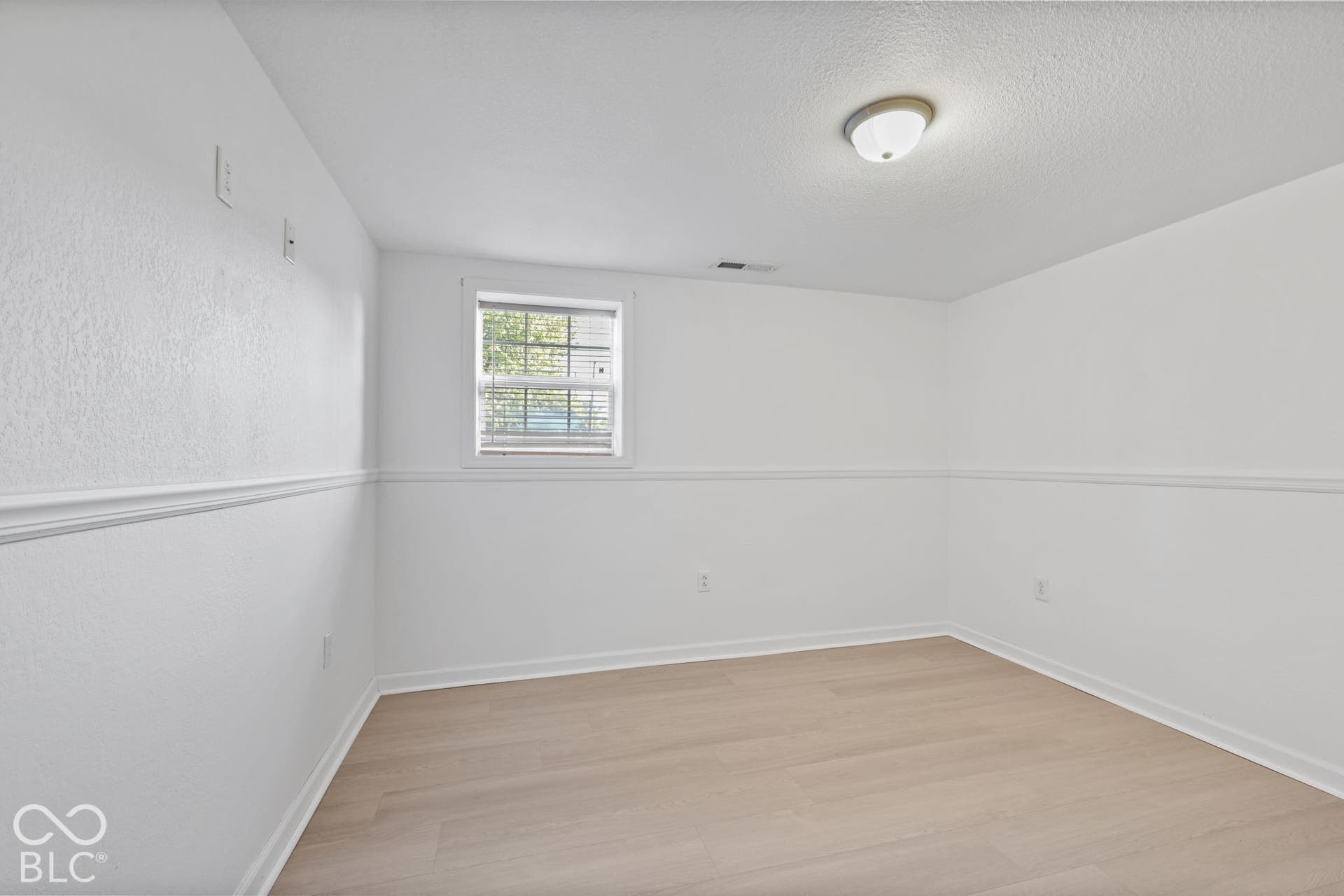 Light wood-finish flooring, white walls with chair rail molding, and a single window with blinds