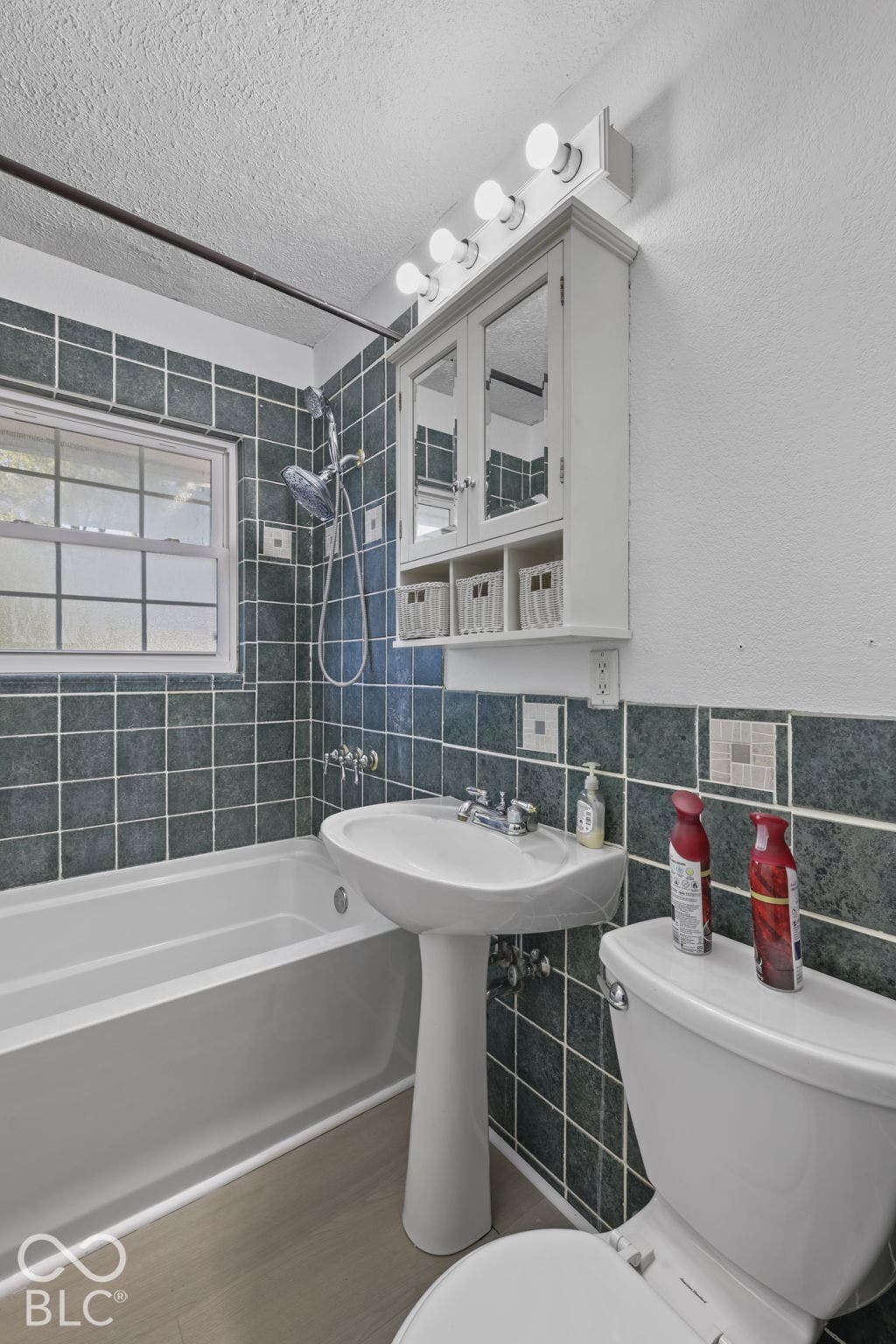 Full bathroom featuring a white pedestal sink, tiled shower surround, recessed window, and white built-in medicine cabinet with integrated lighting