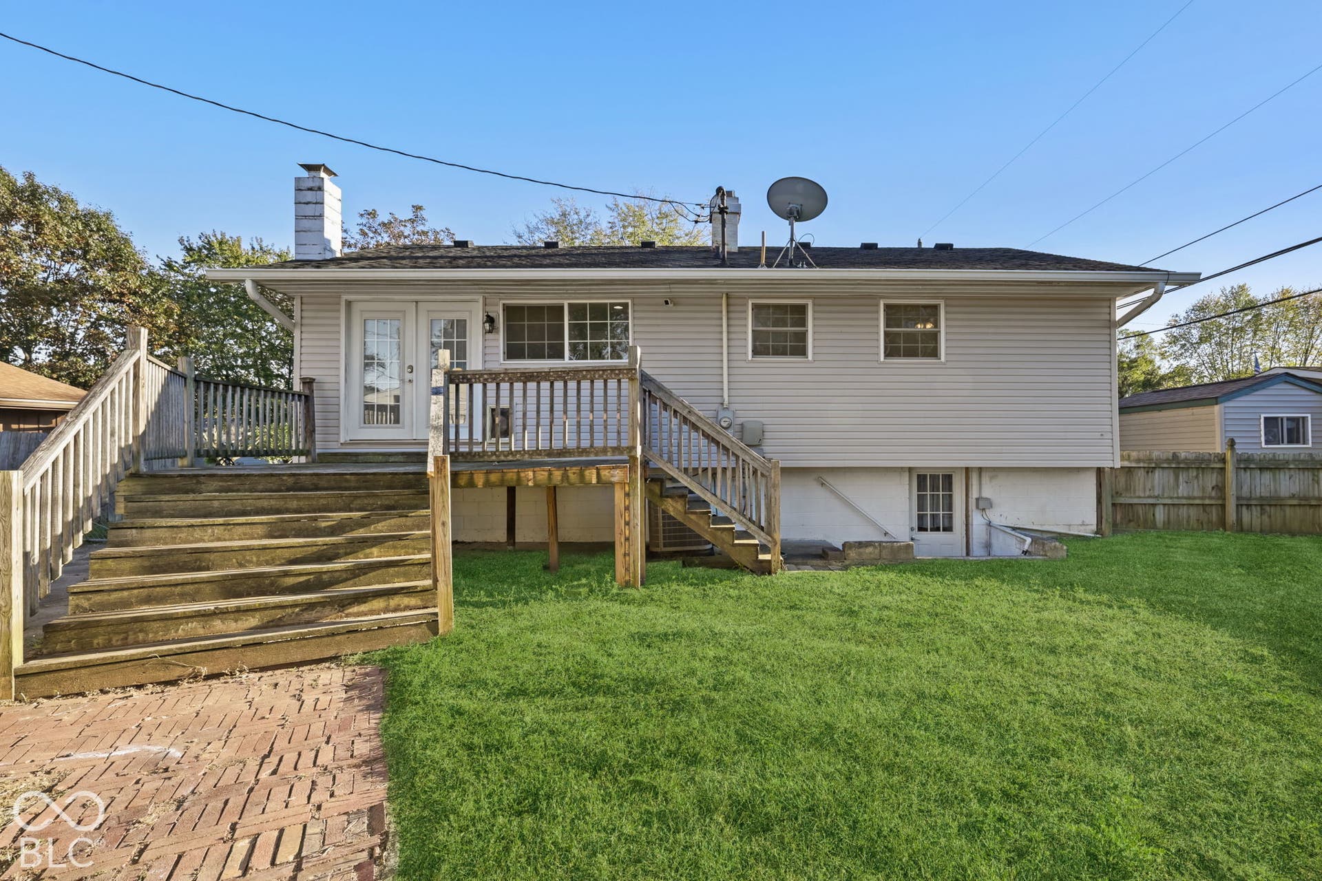 Virtually Altered - Backyard featuring a wood deck with multiple entry points, a brick paver patio, a partial privacy fence, and a walk-out basement entry