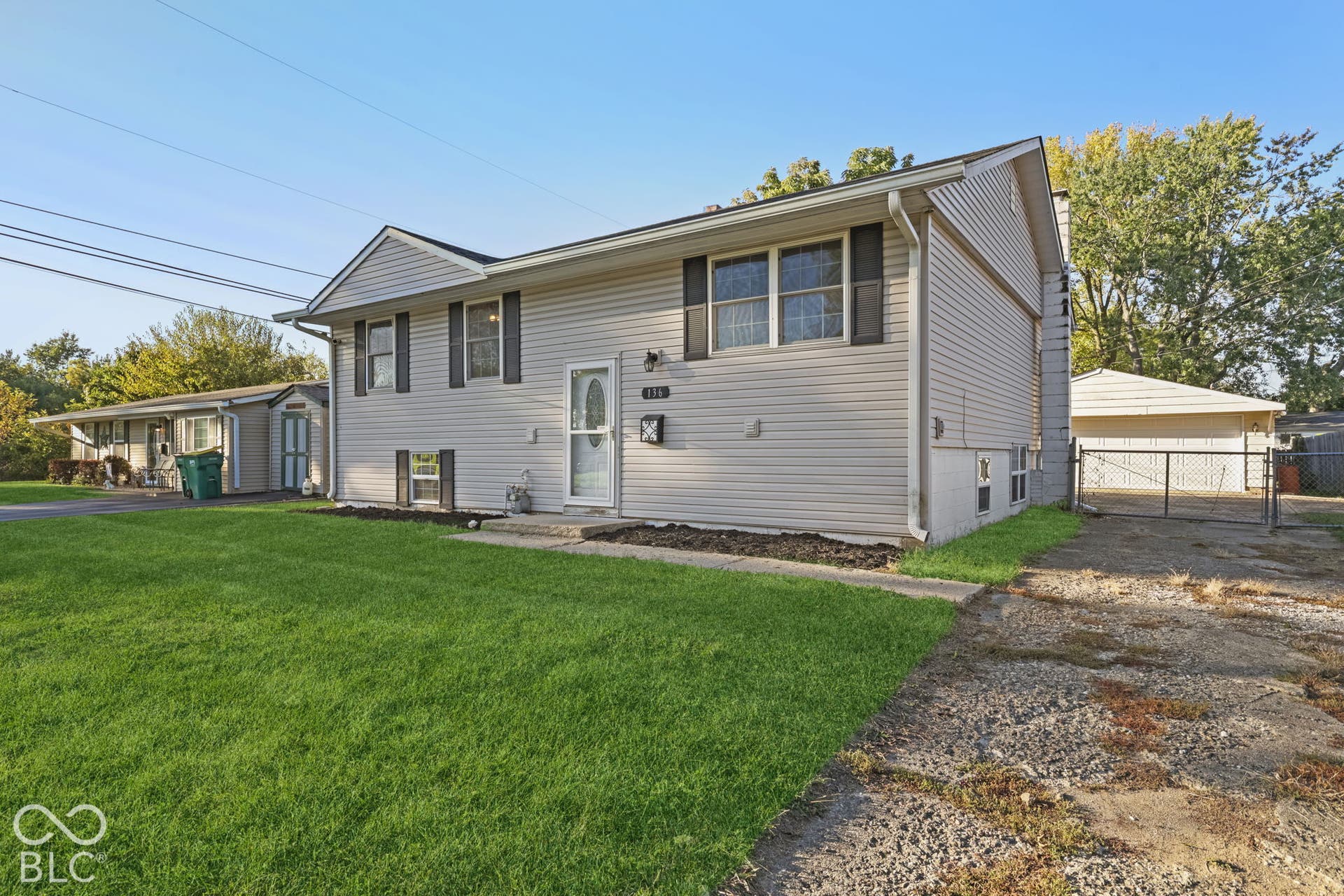 Virtually Altered - Split-level residence featuring light-colored siding, dark window shutters, and a front entry with a storm door