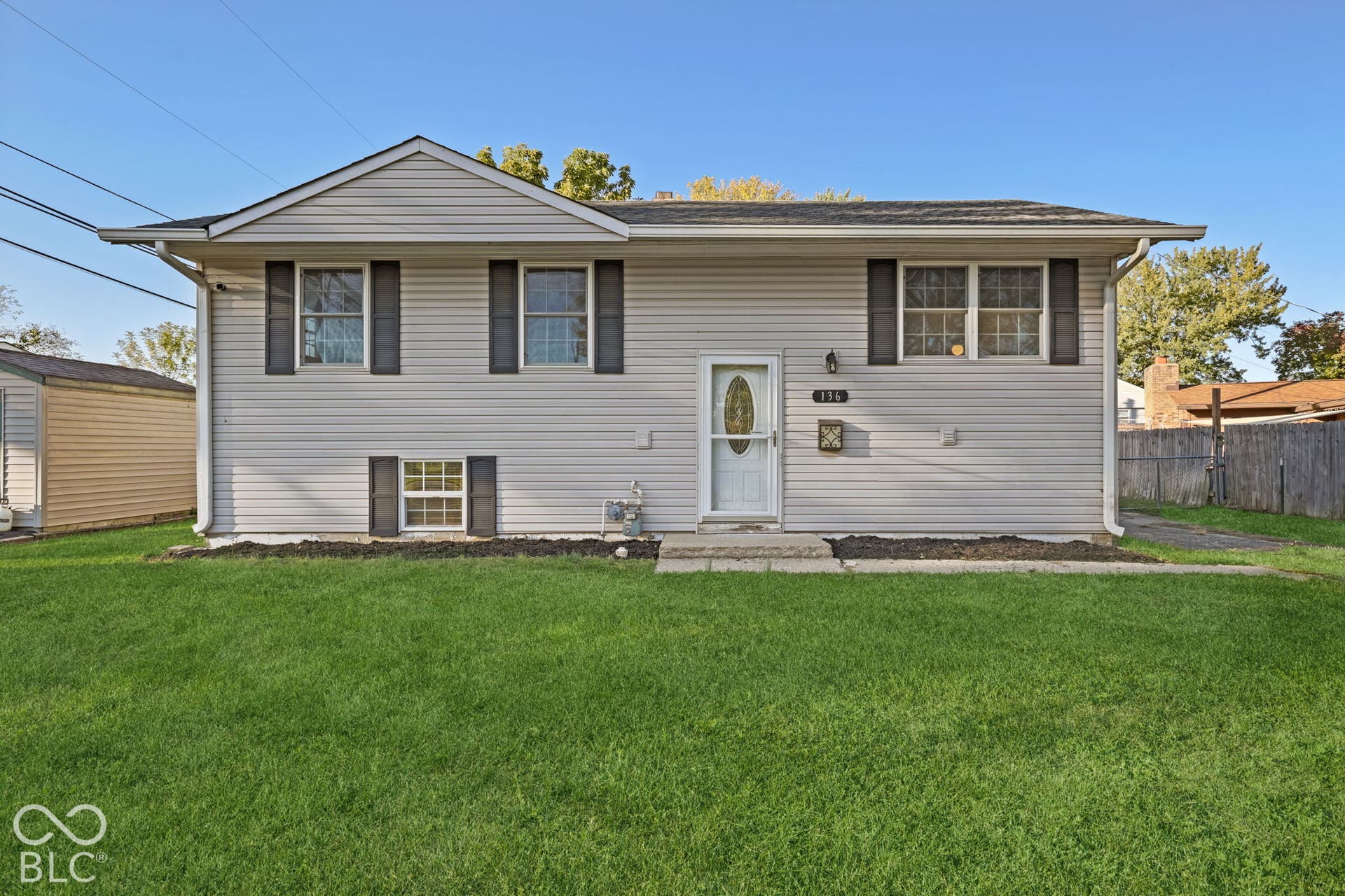 Virtually Altered - Two-story residence featuring light-colored siding, dark window shutters, a front entry door with decorative glass, and a paved walkway