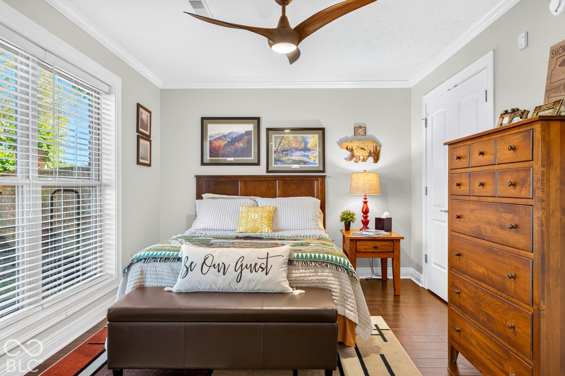 Hardwood flooring, crown molding, double window with blinds, wood-finish ceiling fan, and a wood paneled headboard