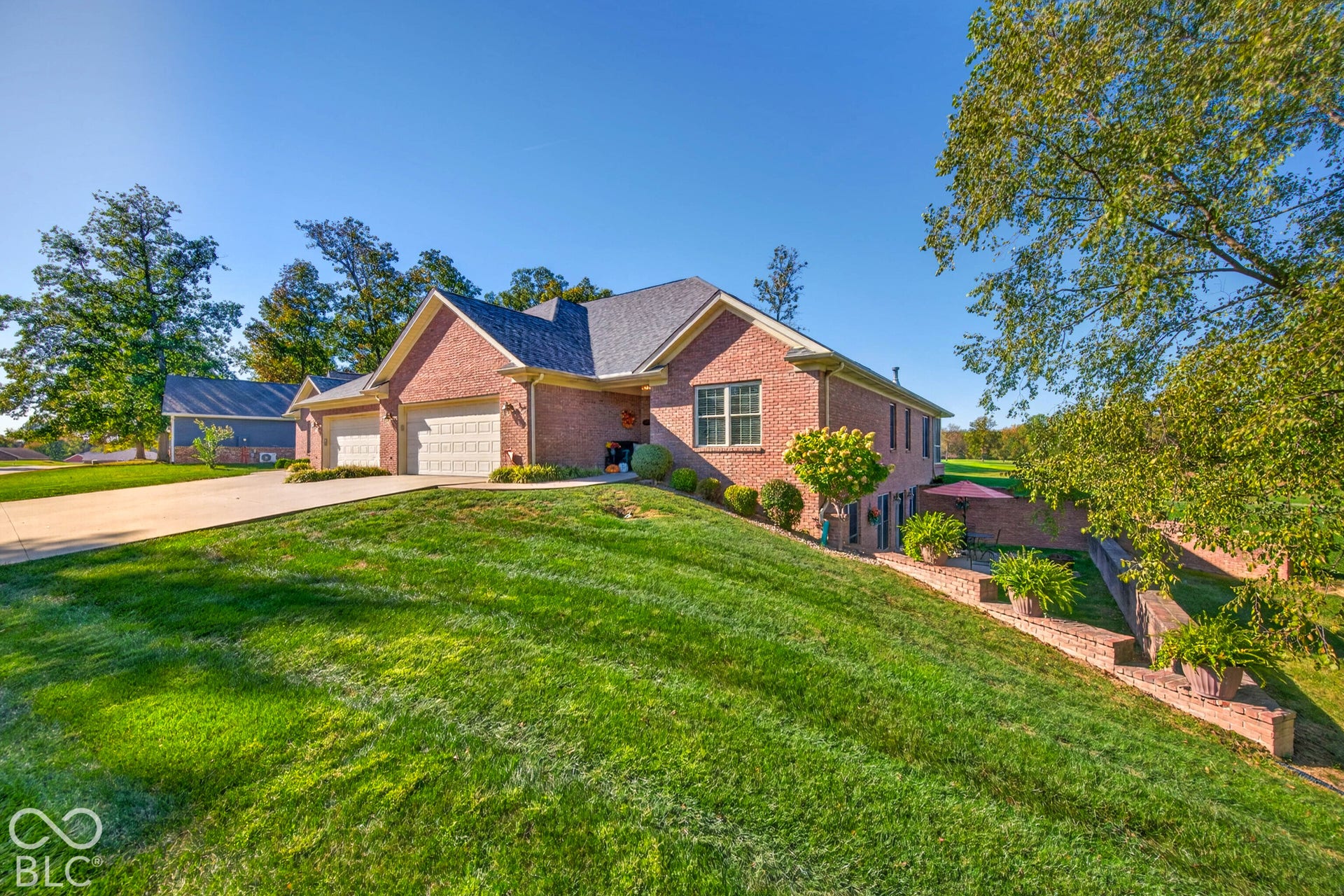 Brick exterior with a multi-car garage, concrete driveway, and established landscaping