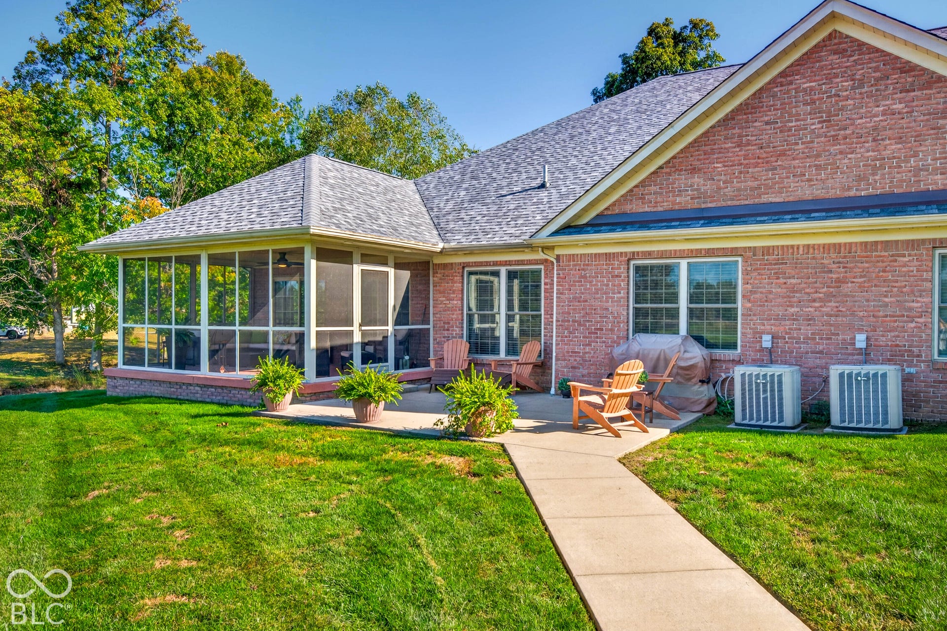 Brick exterior with multiple windows, screened-in porch with ceiling fan, concrete patio, and a well-maintained lawn