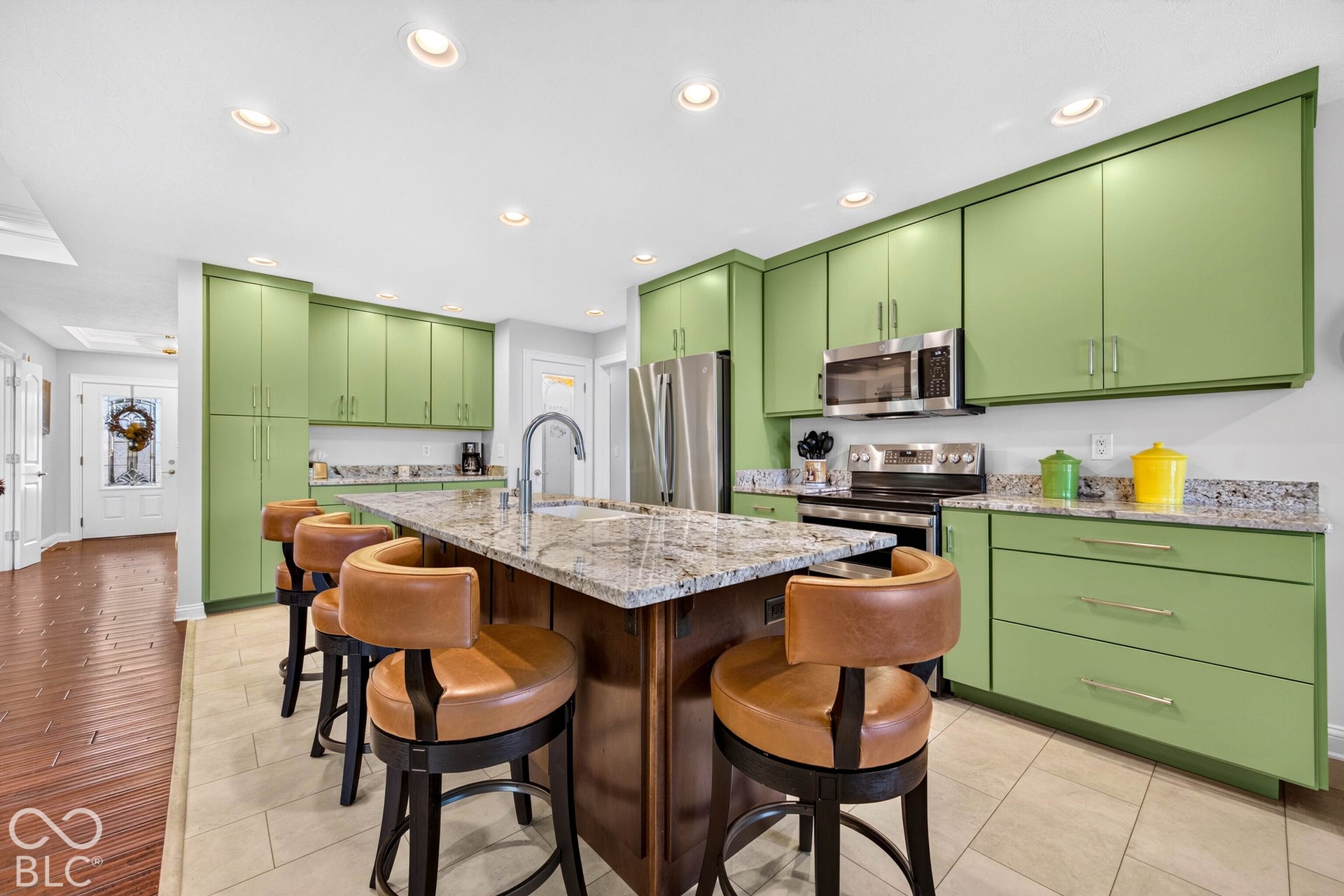 Kitchen featuring an island with a built-in sink, stainless steel appliances, recessed lighting, tile flooring, and wood-finish flooring extending from the entryway