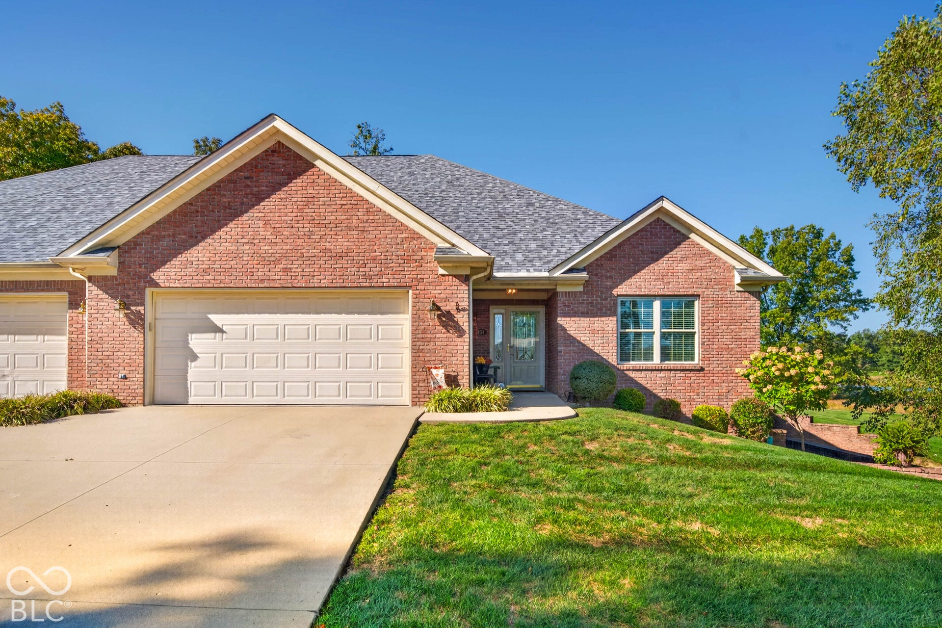 Brick exterior with a gray shingle roof, attached garage, concrete driveway, and front entryway