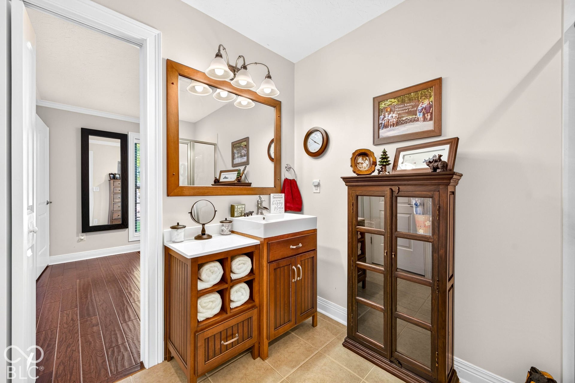 Wood-finish vanity with a rectangular vessel sink, wall-mounted light fixture, and a framed mirror