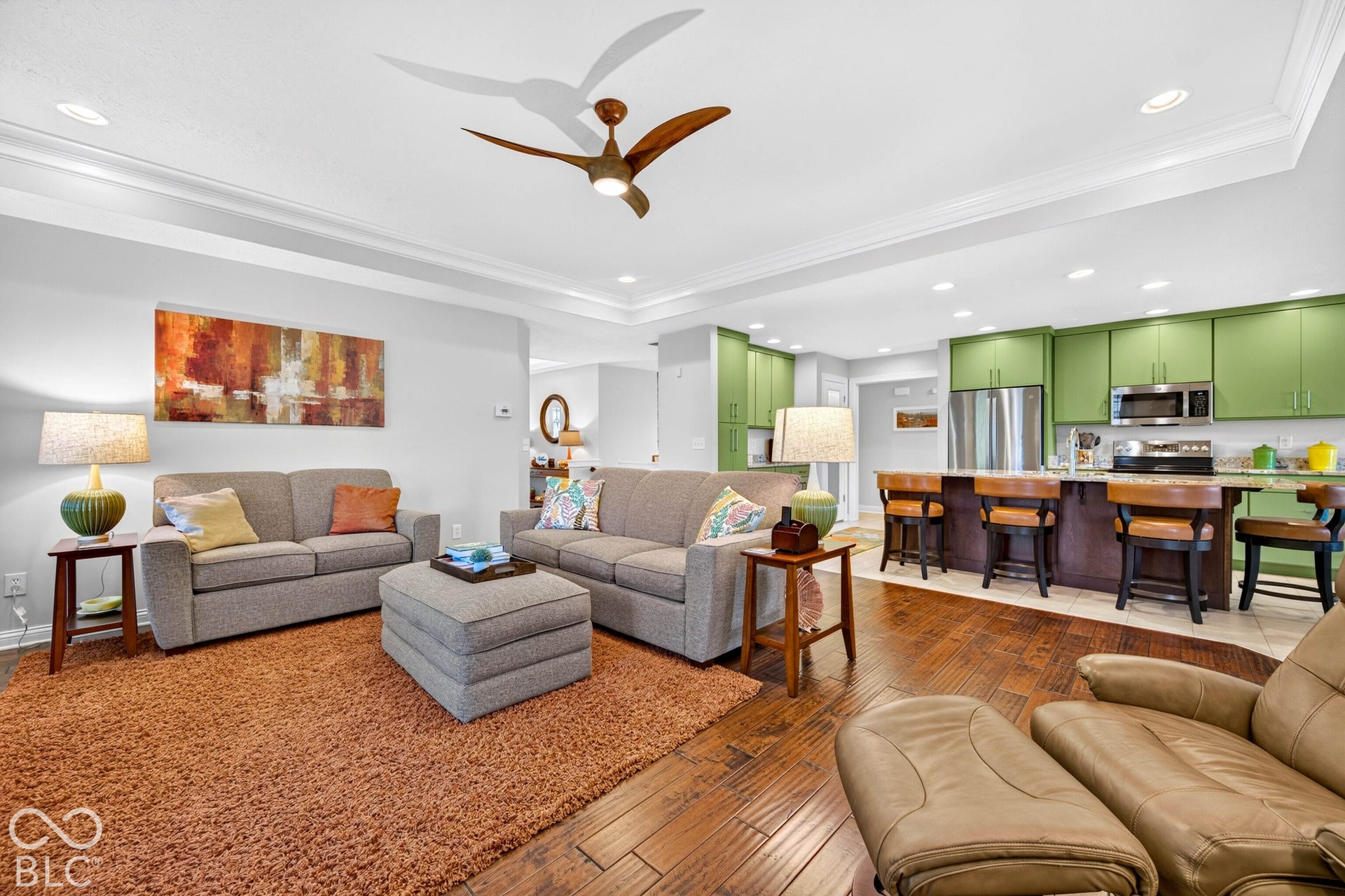Open-concept living area with wood-finish flooring, a tray ceiling, and a ceiling fan