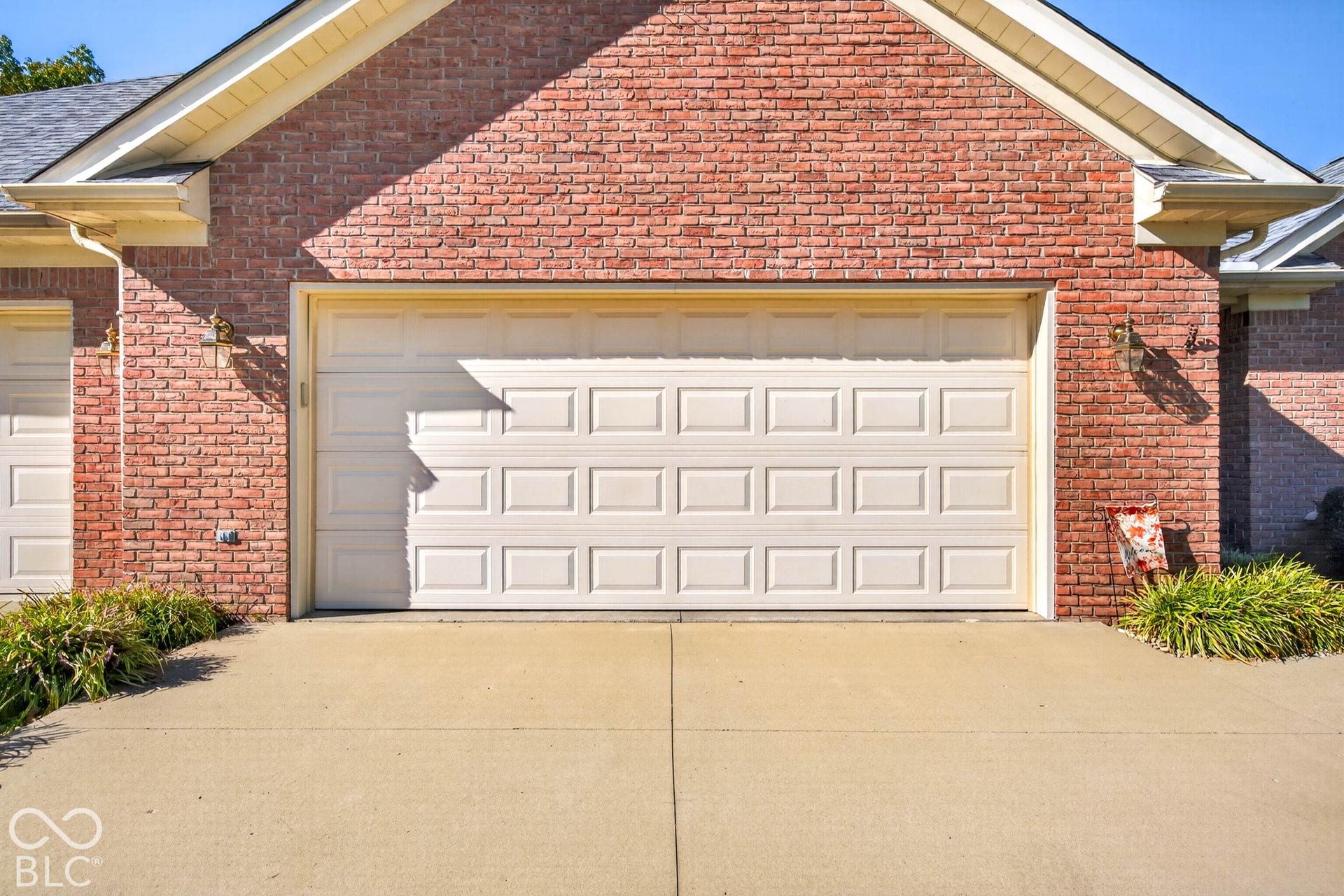 Brick exterior featuring a two-car garage with a panel door, concrete driveway, and established foundation plantings