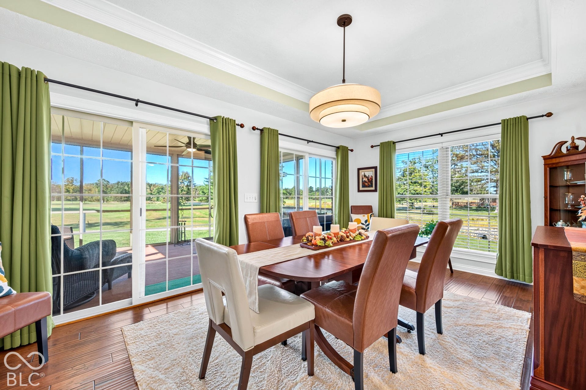 Hardwood flooring, tray ceiling, sliding glass doors, multiple large windows, and a built-in display cabinet