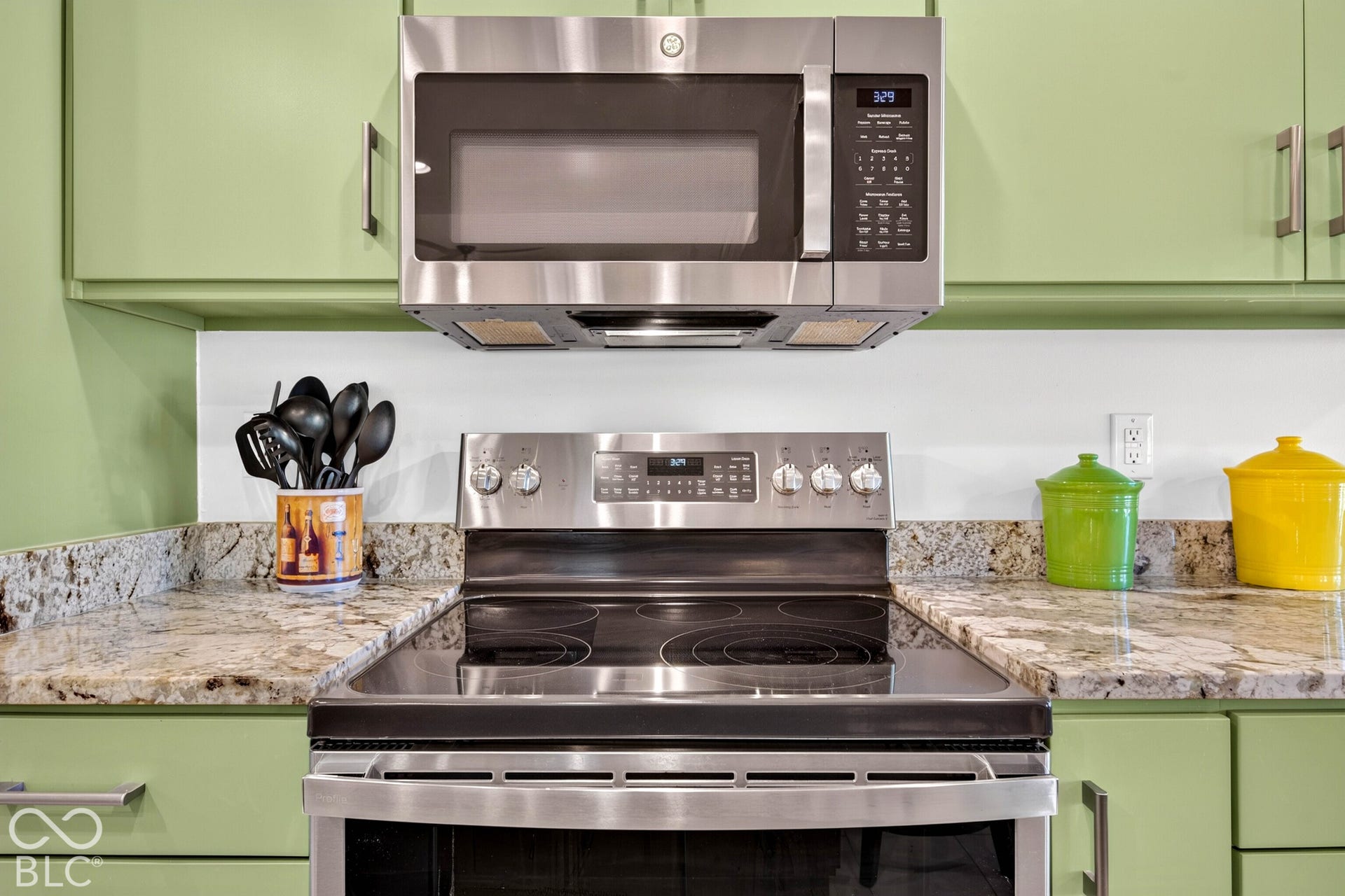 Stainless steel appliances including an oven range and microwave, light green cabinetry, and speckled countertops