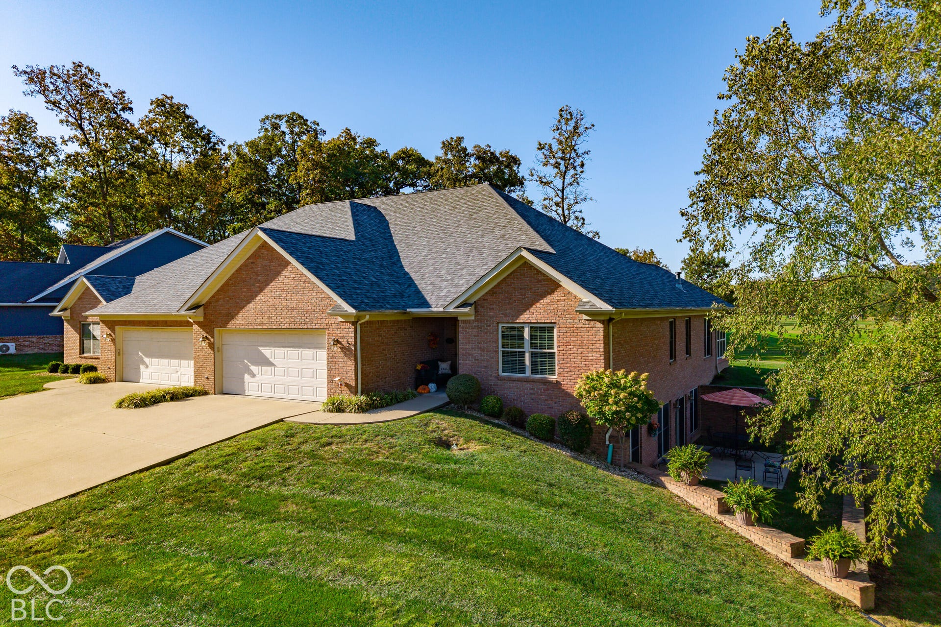 Brick exterior, two-car garage, pitched shingle roof, established landscaping, and terraced outdoor area