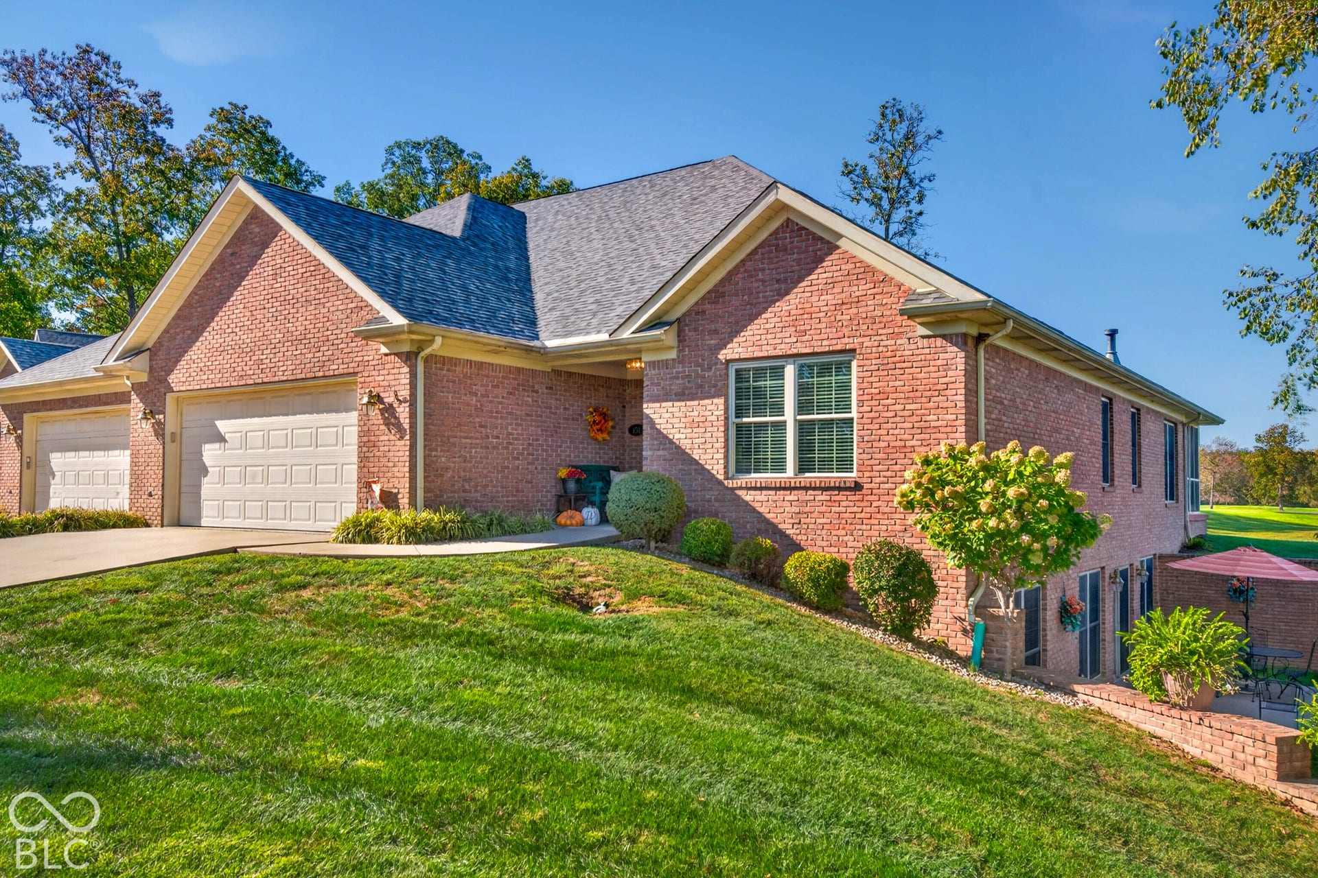 Brick exterior residence featuring a gray shingle roof, two-car garage, and established landscaping