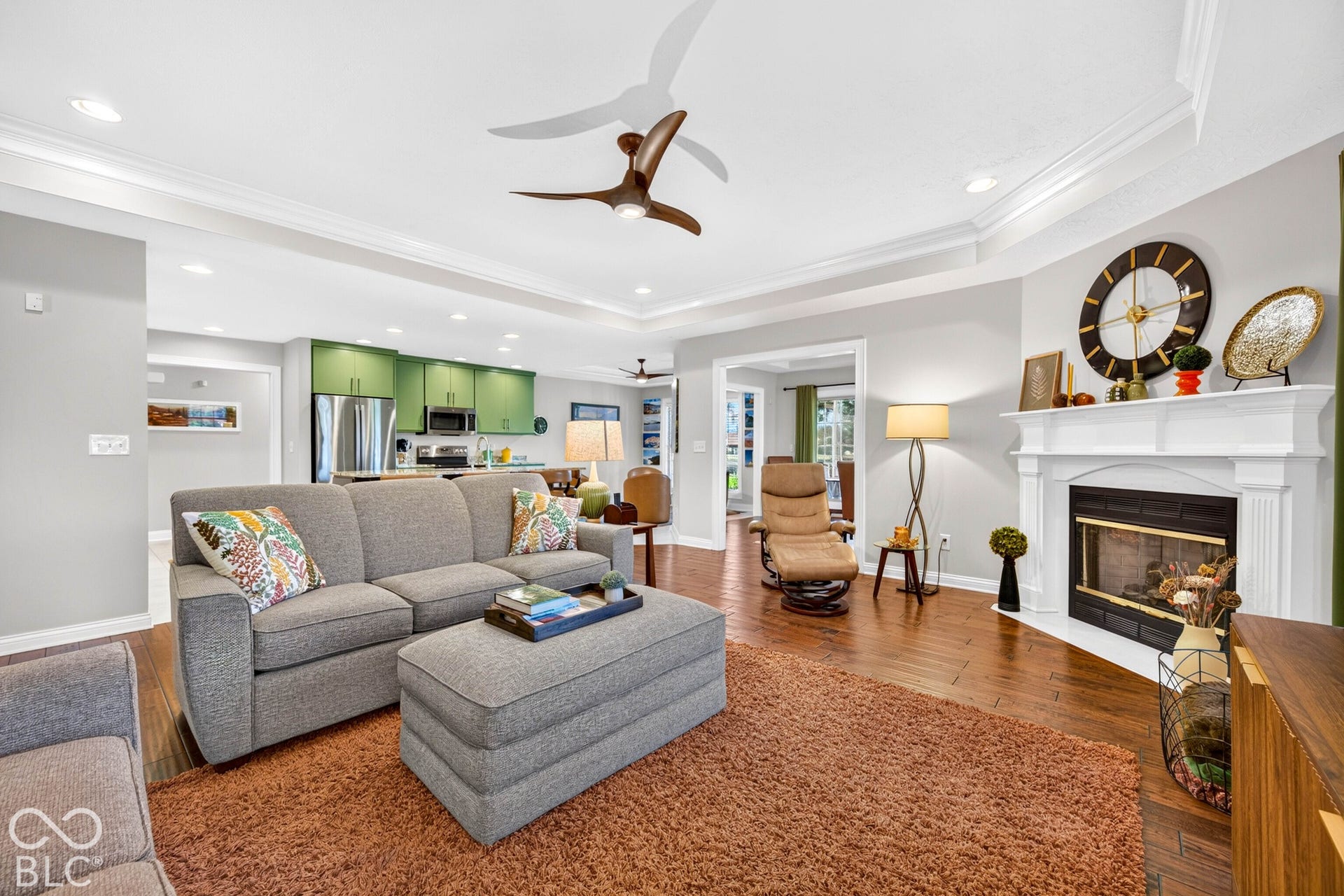 Hardwood-finish flooring throughout, tray ceiling with recessed lighting, and a corner fireplace with a white mantel