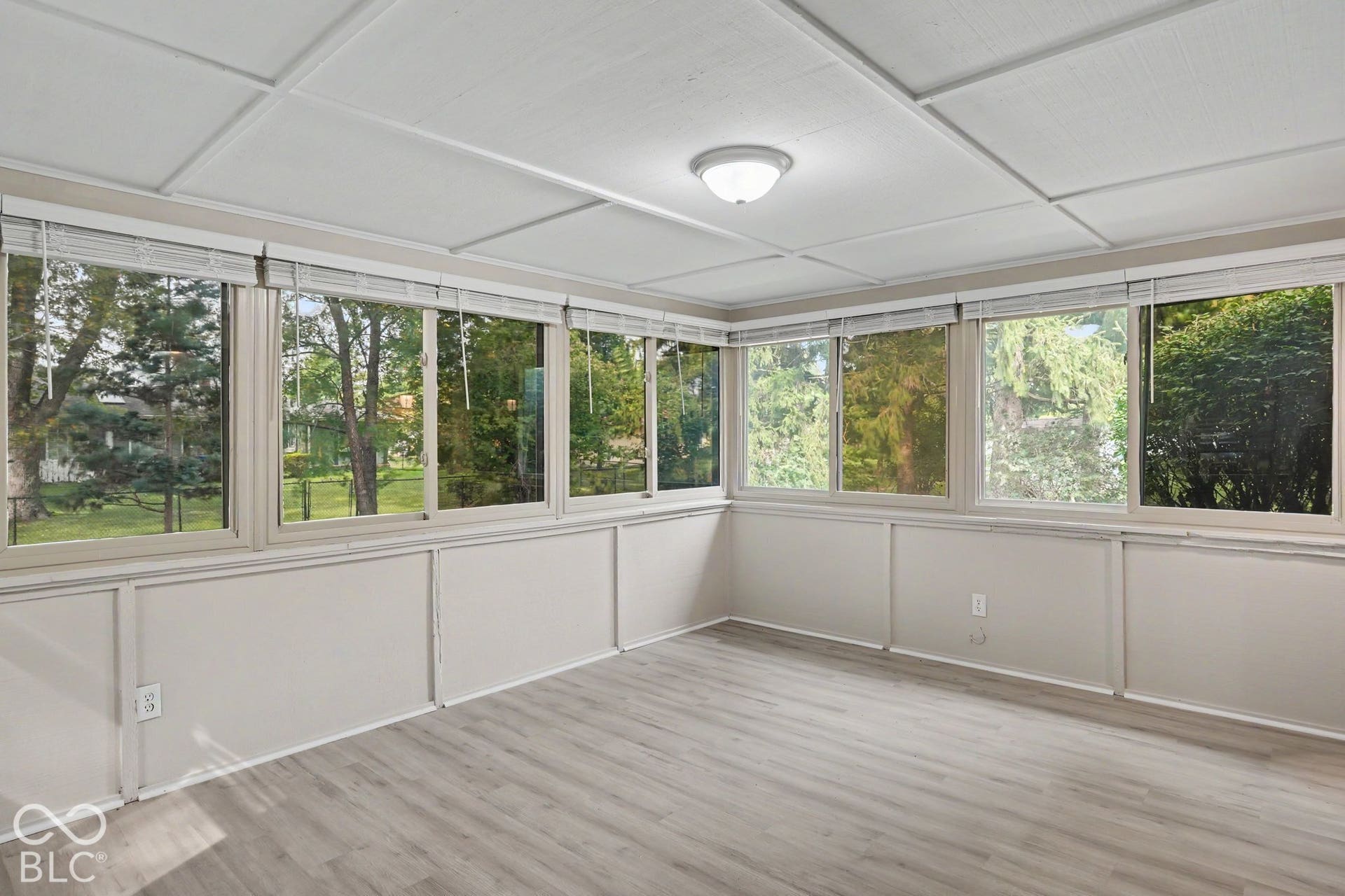 Light wood-finish flooring, numerous windows with blinds, white paneling, and a flush mount ceiling fixture