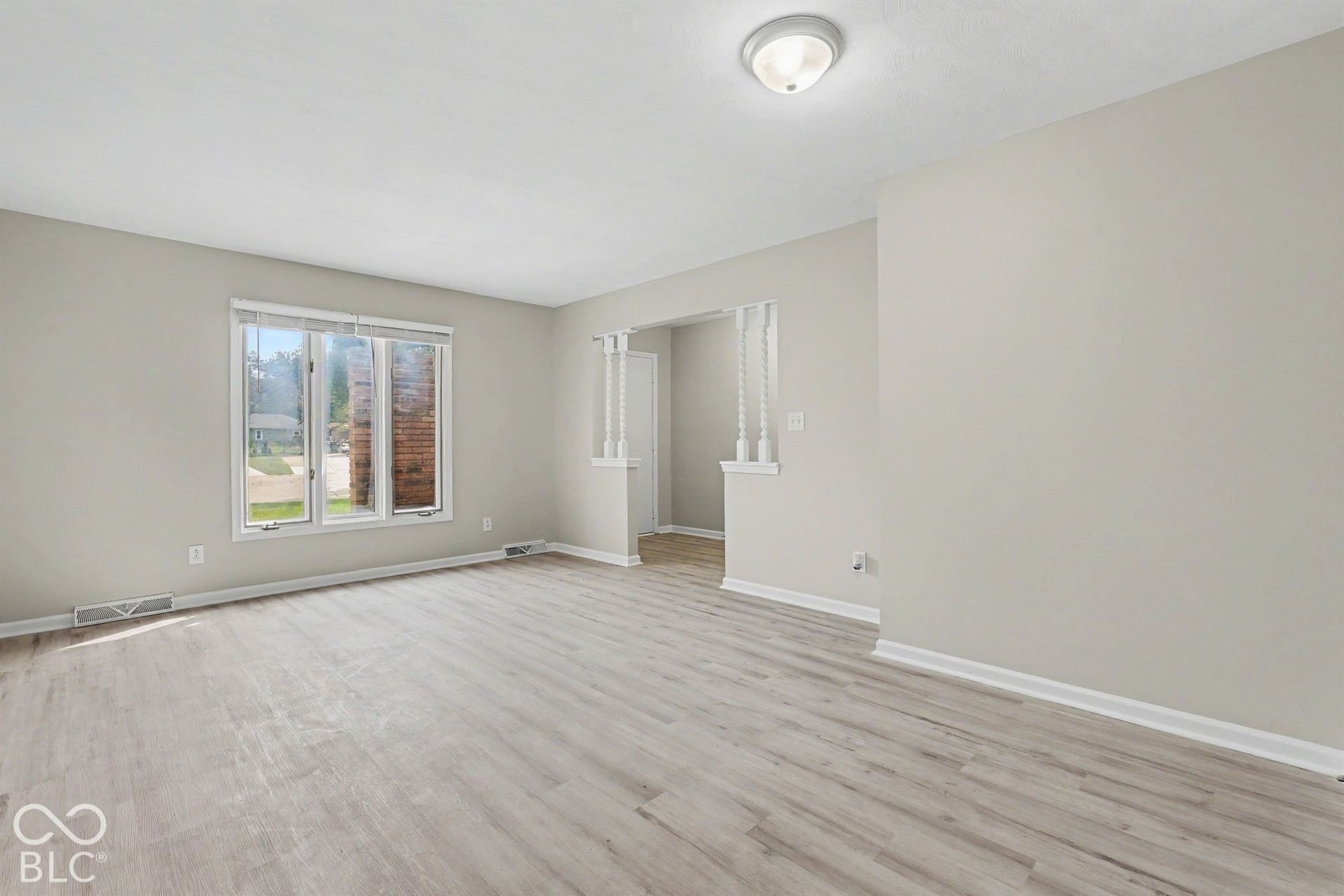 Bright interior with light gray walls, wood-finish flooring, a flush-mount ceiling light fixture, and a multi-pane window