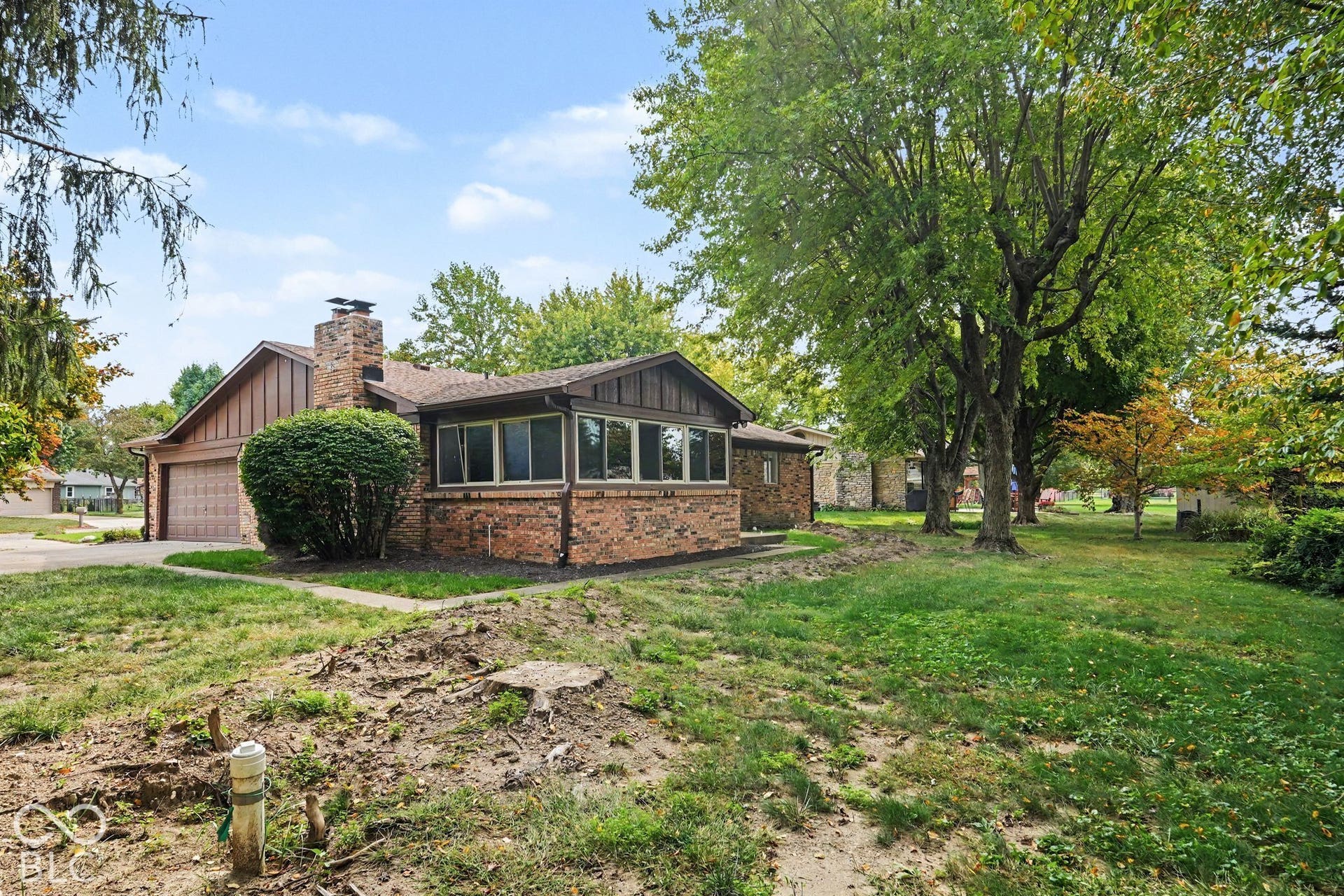 Brick exterior with a prominent chimney, attached garage, multiple windows, and mature trees
