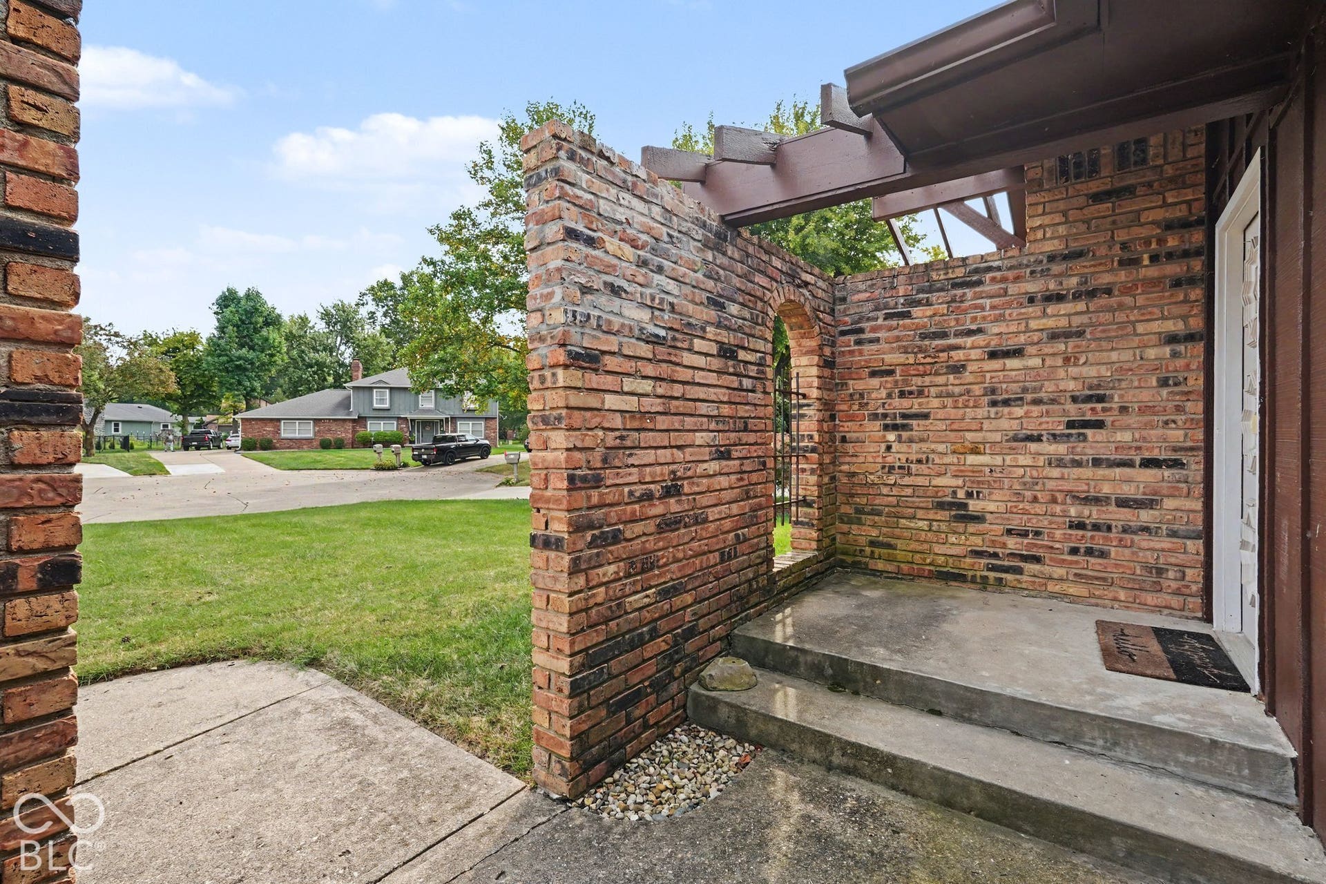 Brick exterior with an arched entryway, concrete steps, and a pergola-style overhang