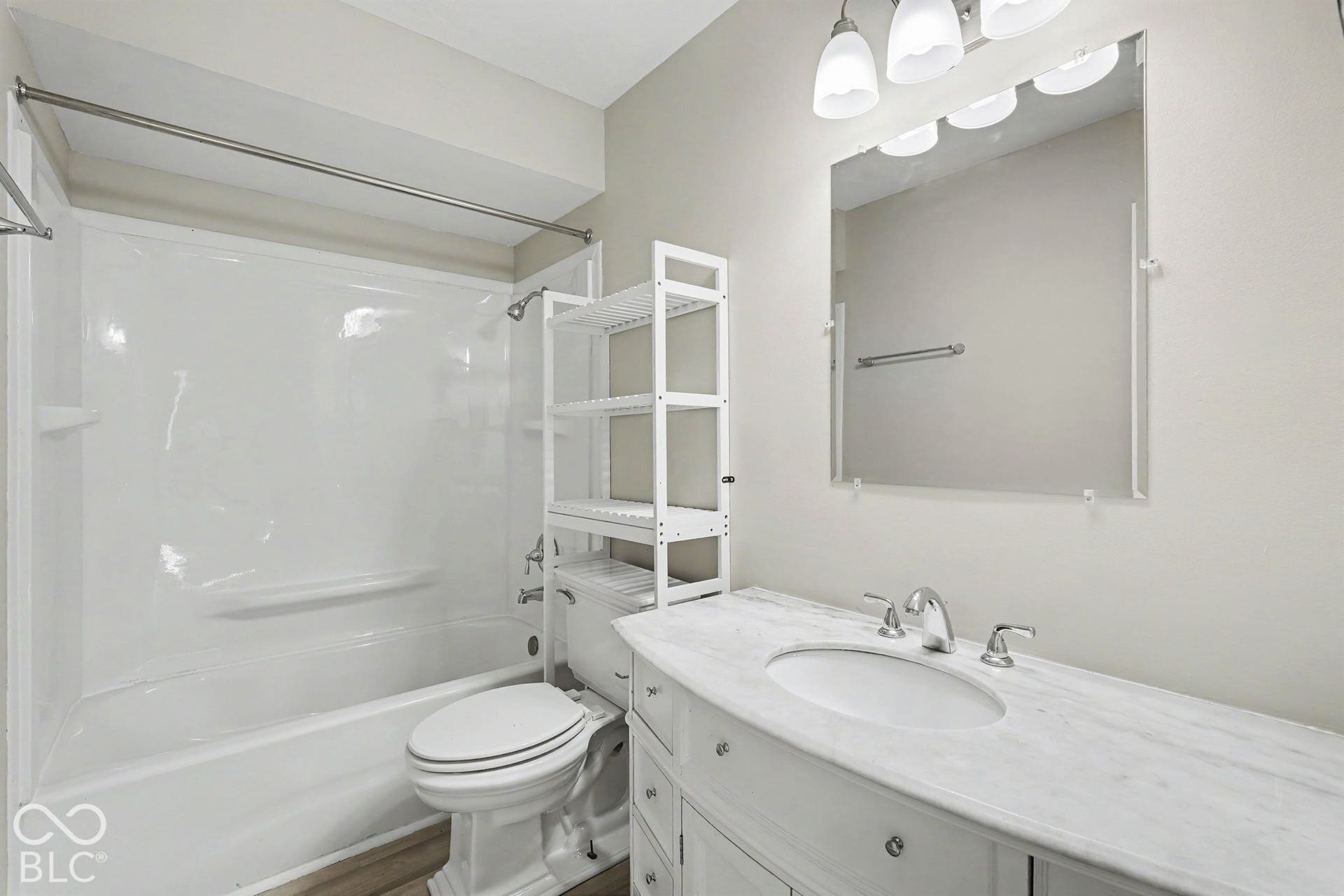 White vanity with a stone countertop, an undermount sink, and a framed mirror with overhead lighting