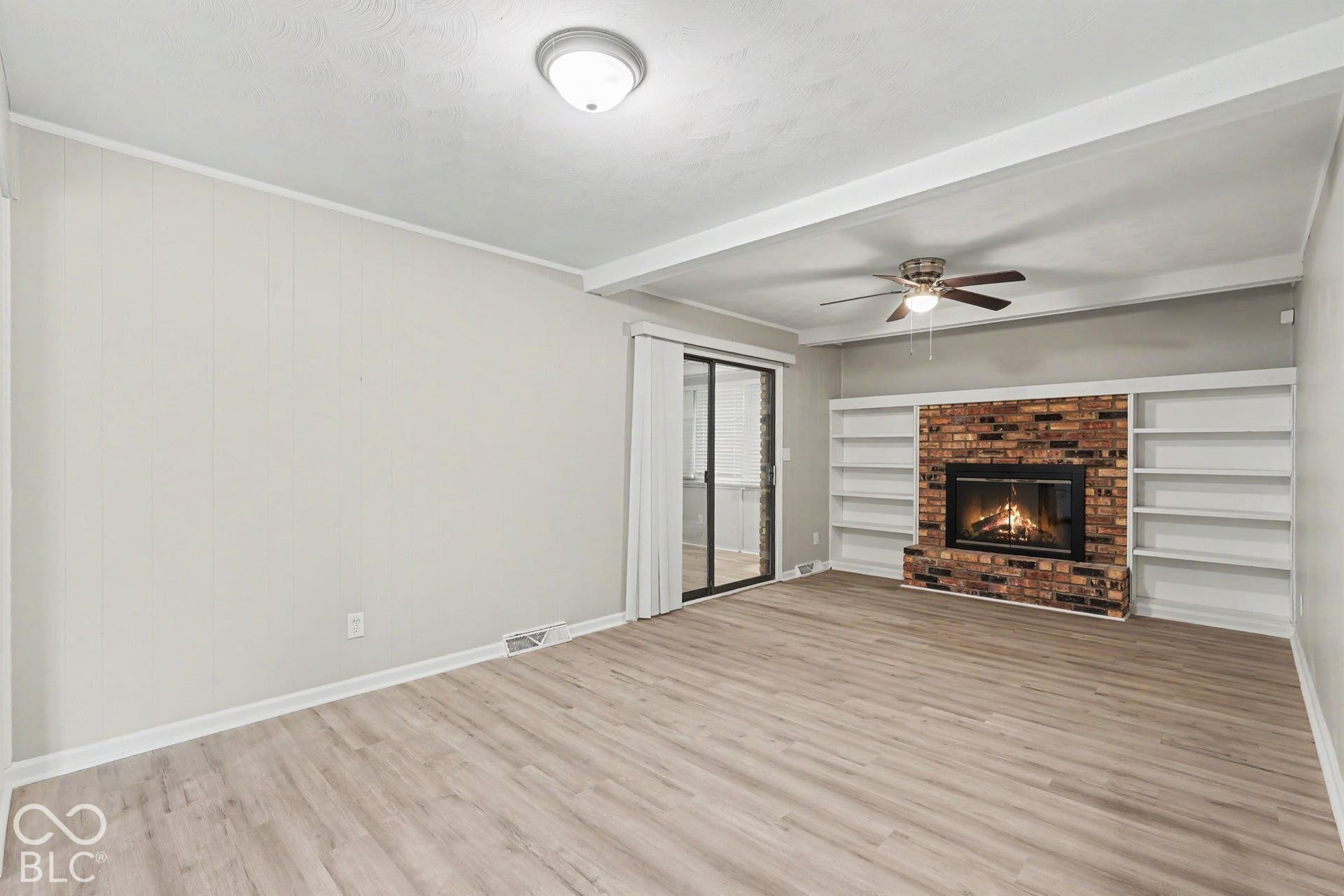 Wood-finish flooring, brick fireplace surround, built-in shelving, ceiling fan, and sliding glass door