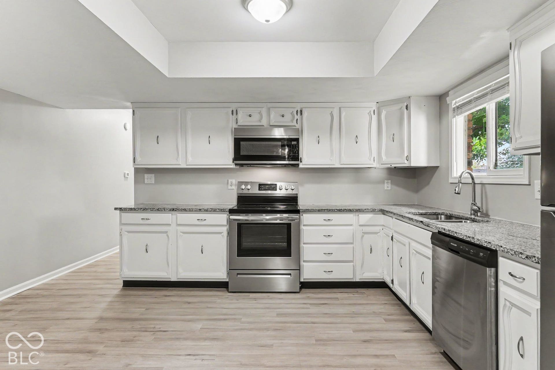 Kitchen with white cabinetry, stainless steel appliances, speckled countertops, and wood-finish flooring