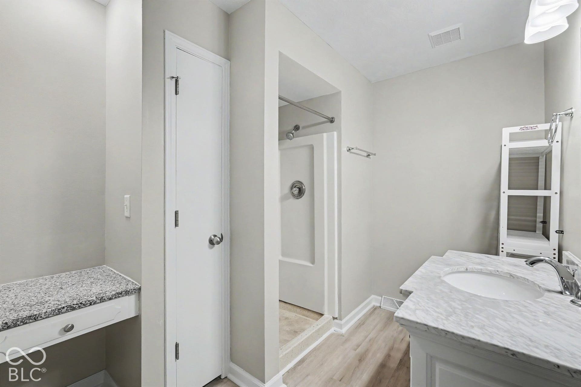 Shower with chrome fixtures, wood-finish flooring, and vanity with an integrated sink and chrome faucet