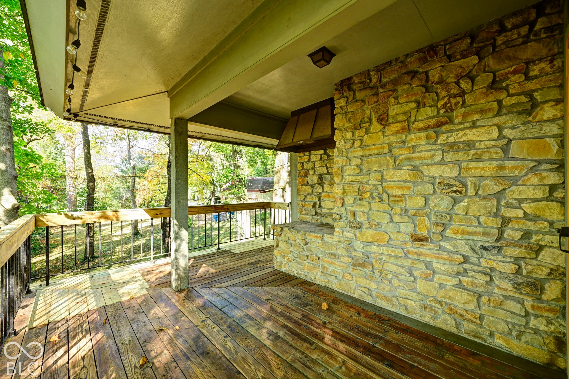 Covered balcony in the treetops with a full stone wall, a built-in stone grill space and deep eaves overhead. Grill out above the ravine. Stone and wood, inside and out, define this organic modern home.