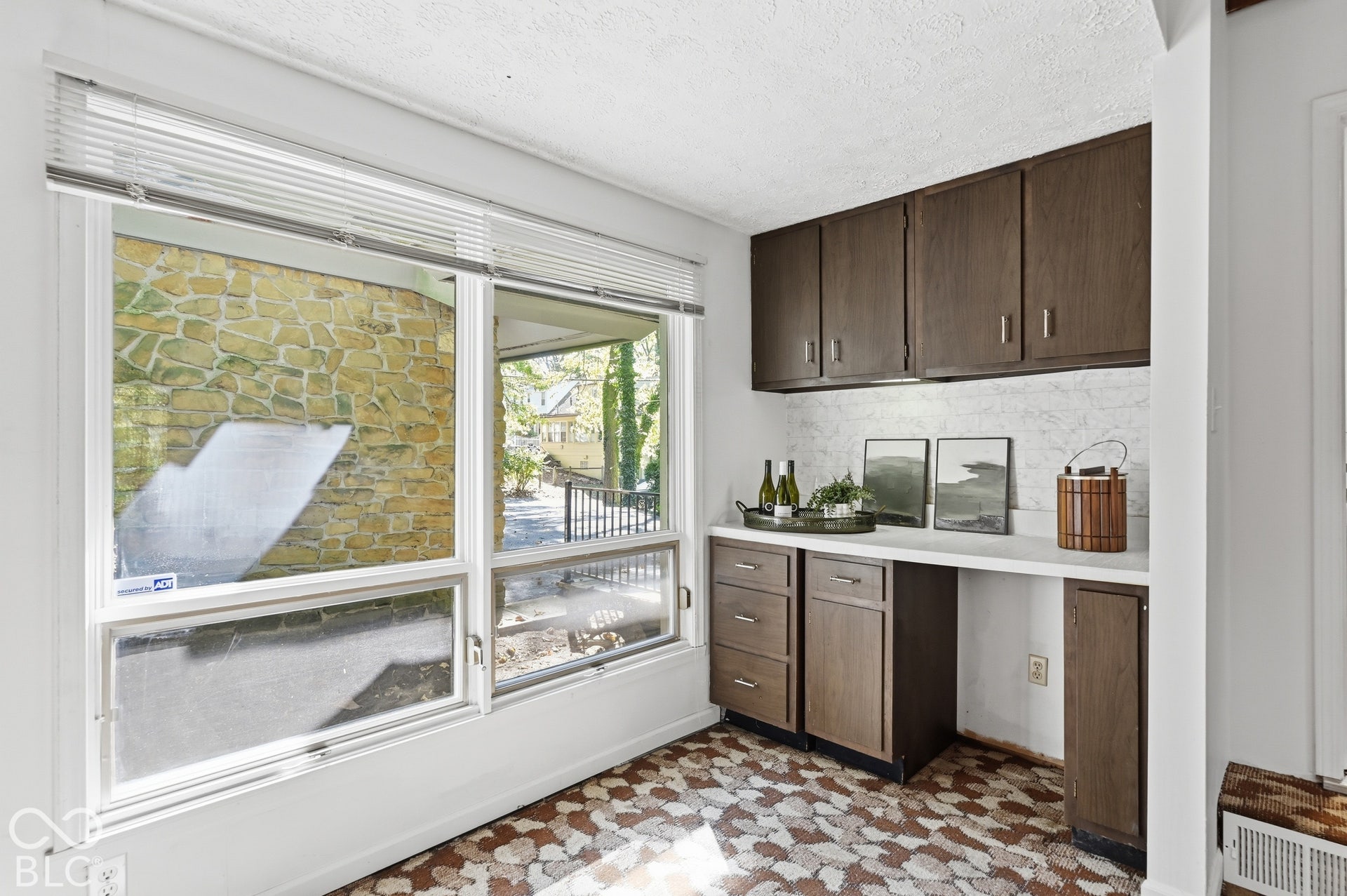 Built-in dry bar with cabinetry and counter beneath a wide window. Original patterned flooring adds authentic midcentury character.