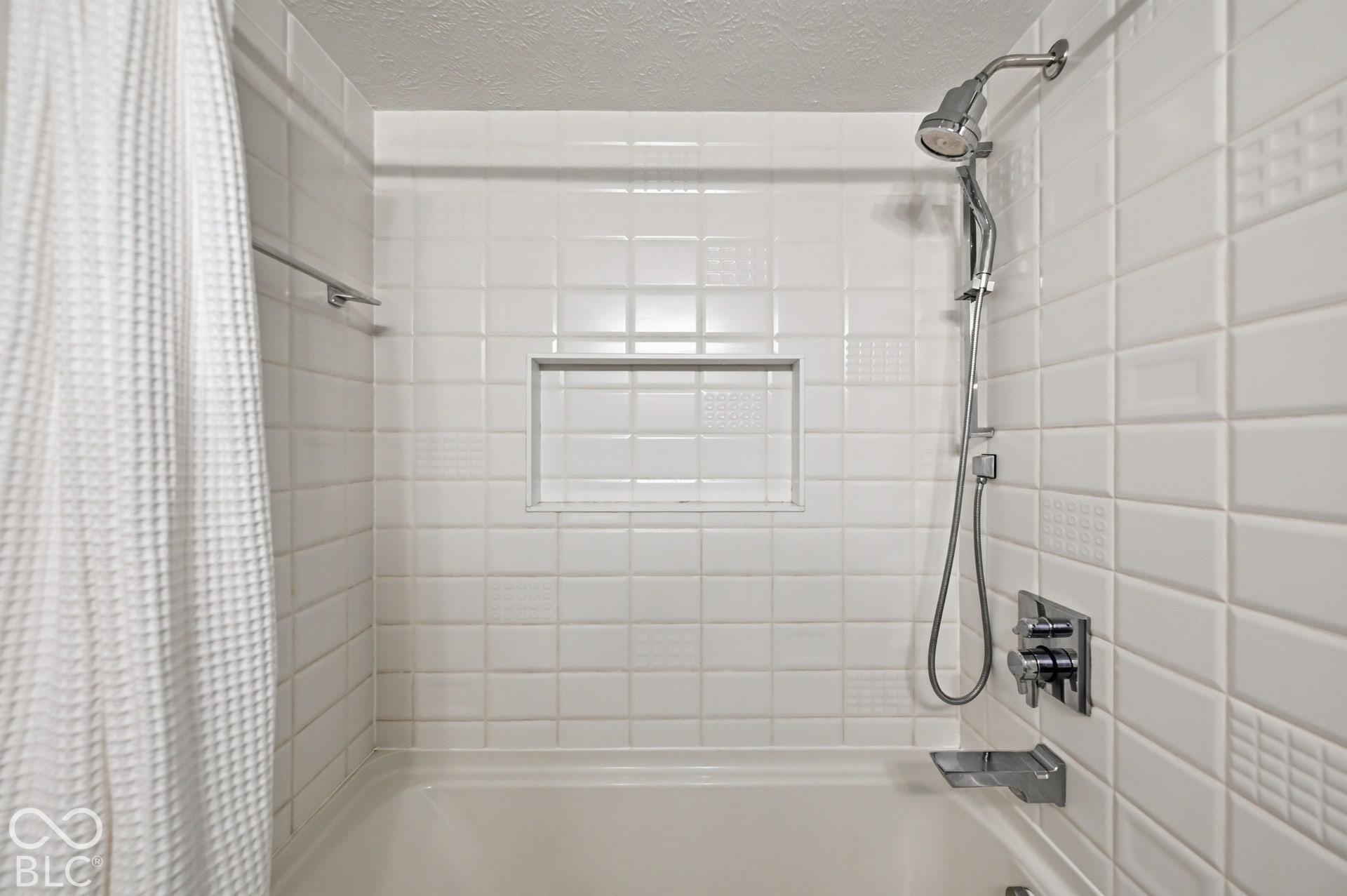 Tub and shower with crisp white tile, built-in niche and rain-style shower head.