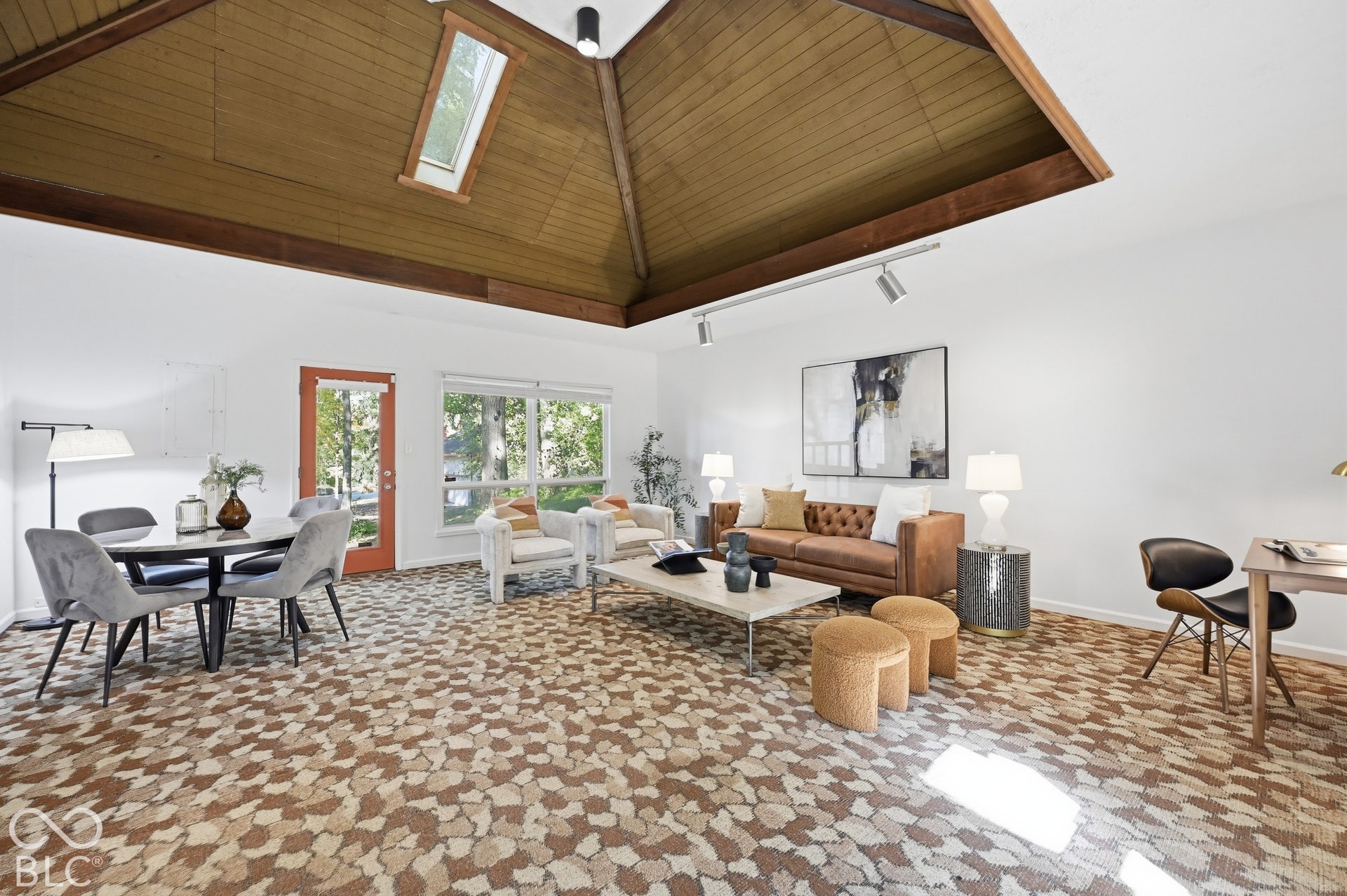 The family room Clyde E. Woods added in 1974: a recessed wood pyramid ceiling with skylight crowns a room made for gatherings, with windows to the woods and a door to the patio.