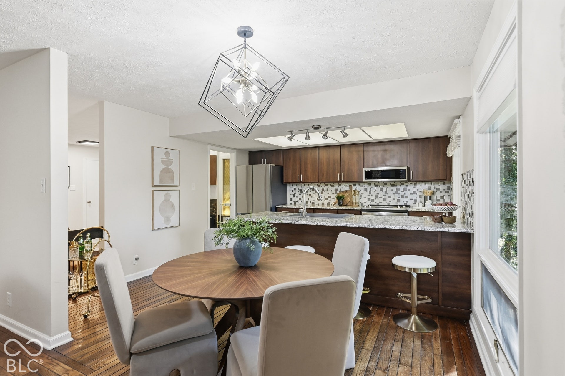 Dining area open to the updated kitchen, with a geometric pendant overhead and corner windows pulling the trees inside.