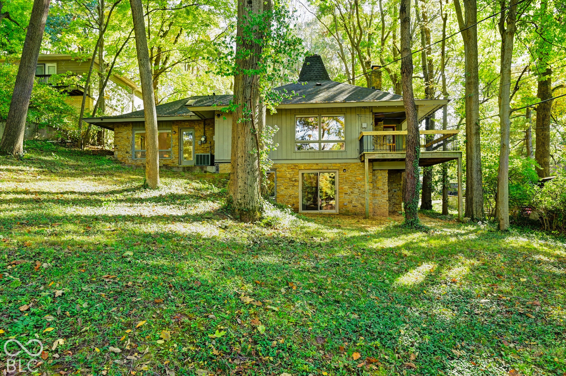 From the backyard, the house rises from the ravine in stone, wood and glass, with the covered balcony set among the trees. Architect-designed midcentury modern in Washington Township.