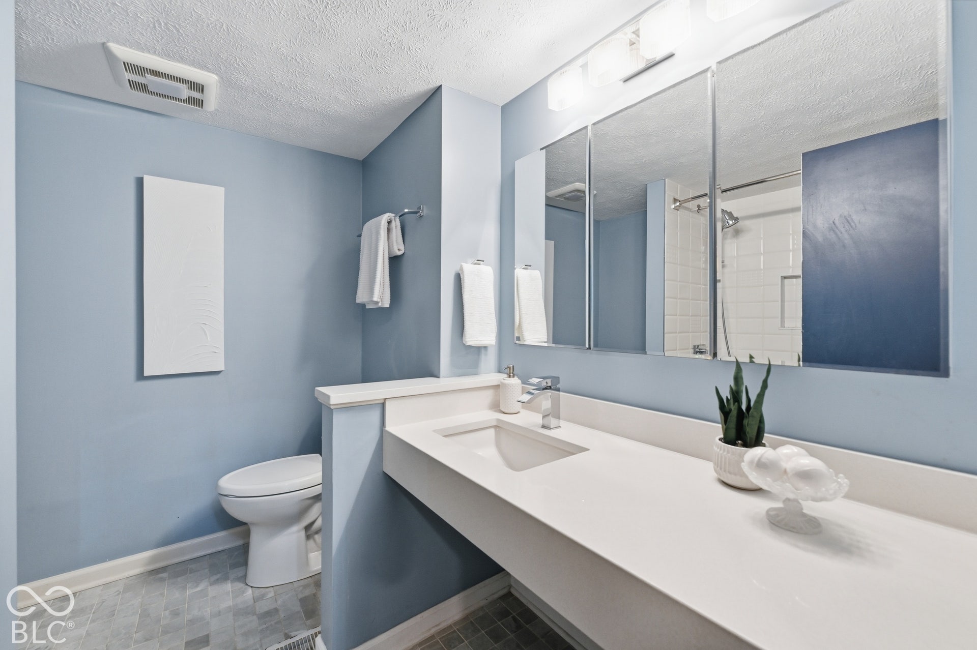 Updated full bath on the bedroom level with a long vanity, wide mirror and soft blue walls.