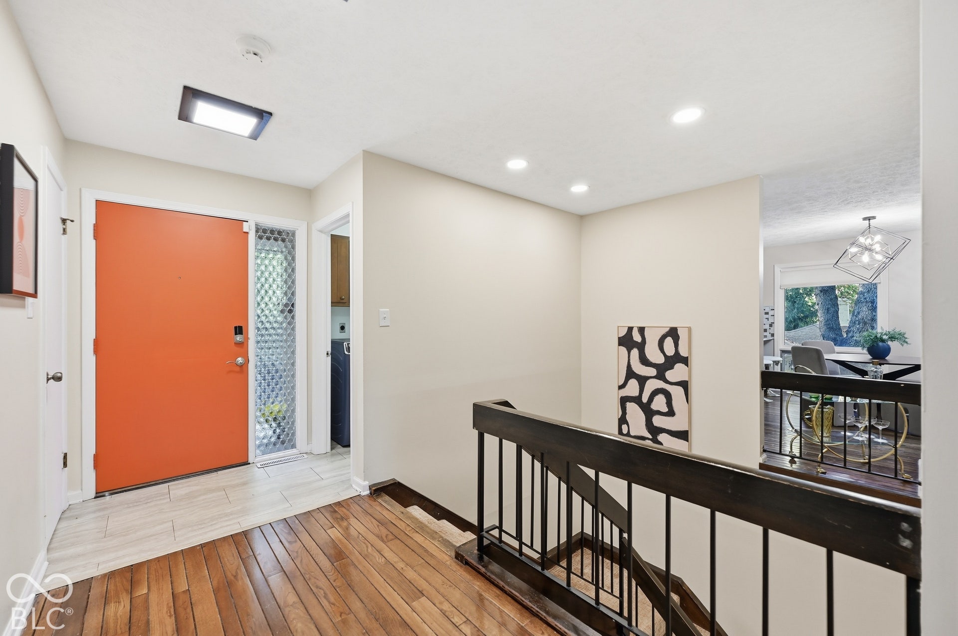 A bold orange front door opens to warm hardwood and an open view across the main level. Just inside, the floating staircase drops to the bedroom level, a signature of Clyde E. Woods' 1967 design.