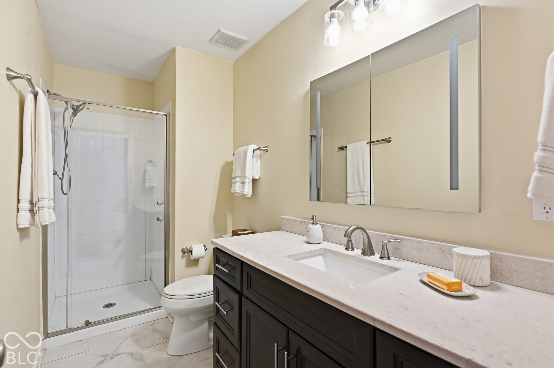 Updated primary bath with a walk-in glass shower, stone-look vanity top and LED-lit mirror.