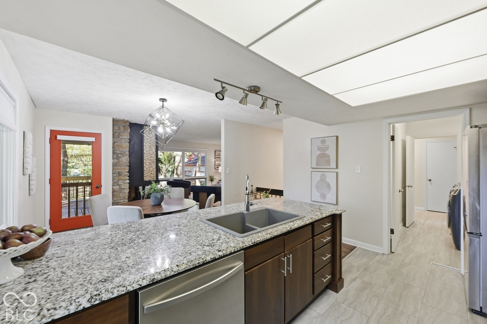 Kitchen, dining and living in one view, with the orange balcony door and stone fireplace beyond. The open plan Clyde E. Woods drew in 1967 still feels modern today.