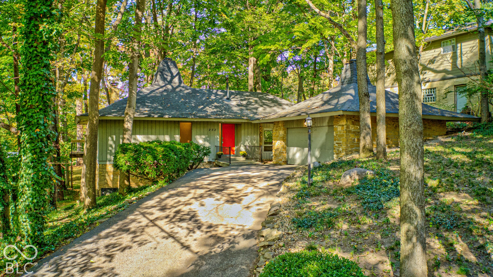 Sweeping pyramidal rooflines and stone walls among mature trees: the Woods House, a 1967 Clyde E. Woods design in north Butler-Tarkington, Indianapolis 46208, with an attached 2-car garage.