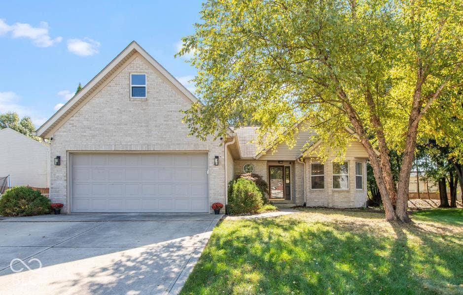 Light brick exterior, attached two-car garage, concrete driveway, and mature landscaping